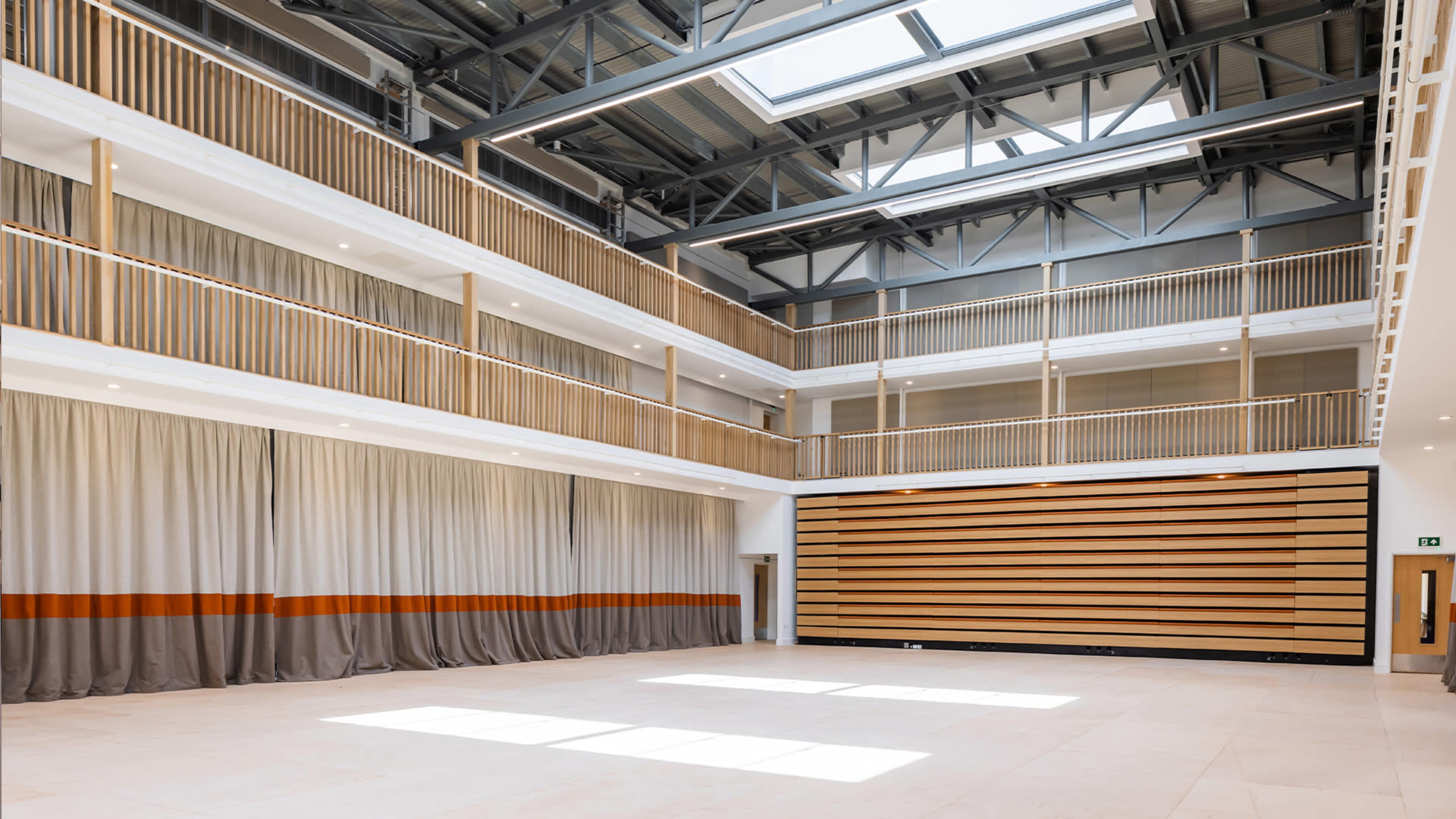 A spacious indoor venue with multiple levels, featuring wooden railings, large curtains, and a wall lined with wooden panels.
