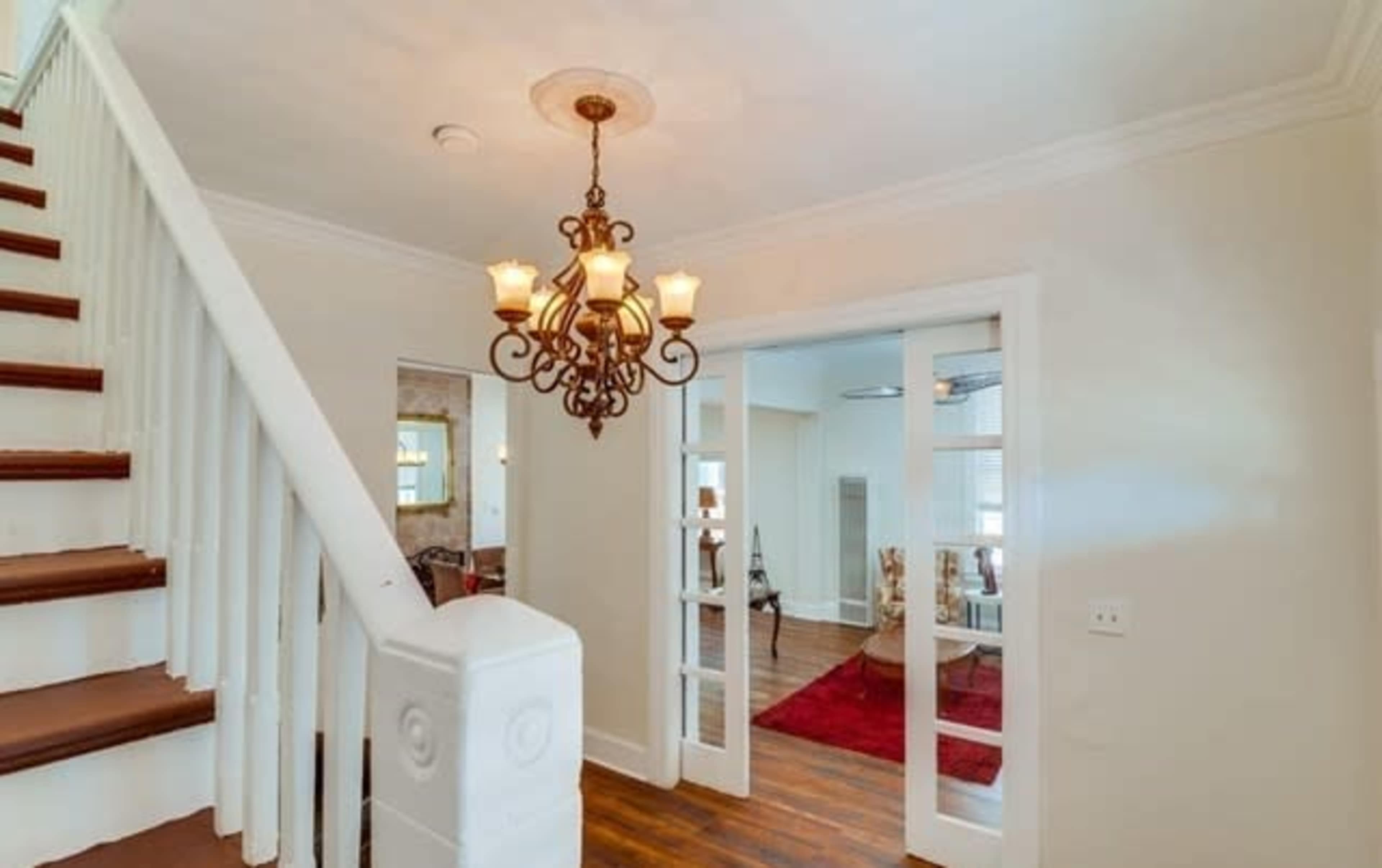 A staircase leads to a well-lit hallway featuring a chandelier and glass-paneled doors opening to a living area.