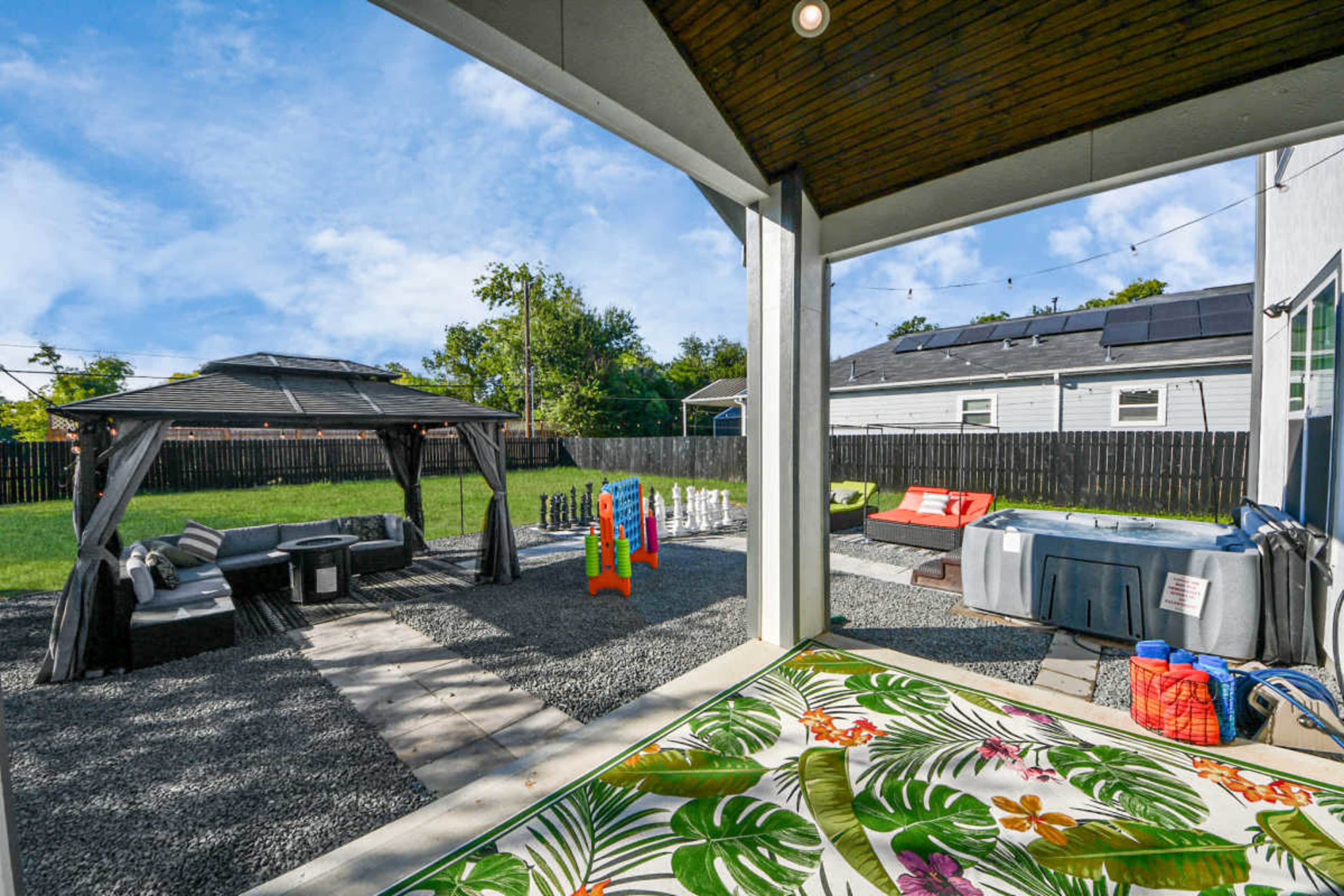 The image shows a backyard scene featuring a gazebo, a hot tub, colorful play equipment, and a seating area, all surrounded by grass and a gravel patio.
