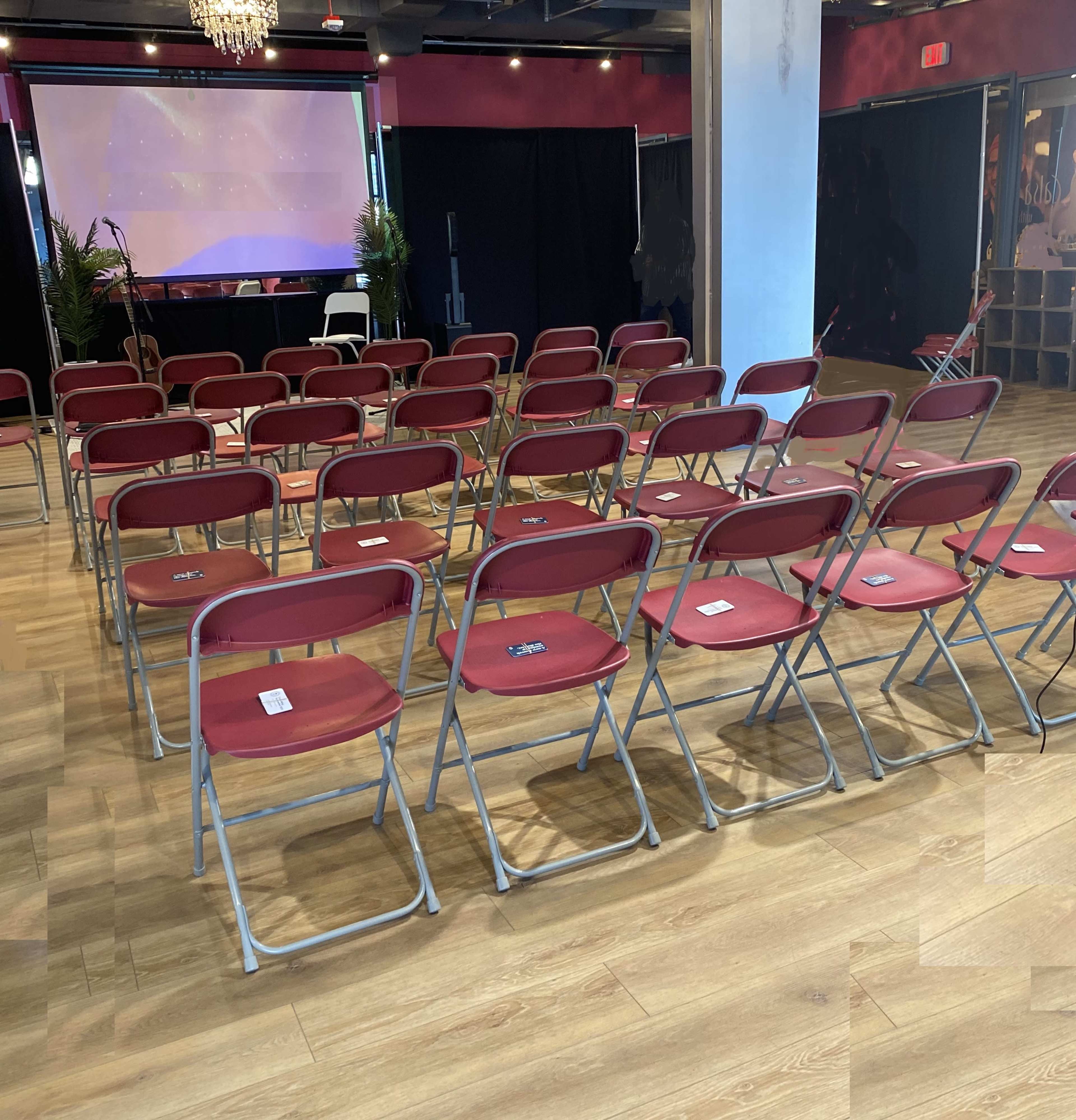 A room set up with rows of red folding chairs arranged facing a presentation screen, with black curtains in the background.