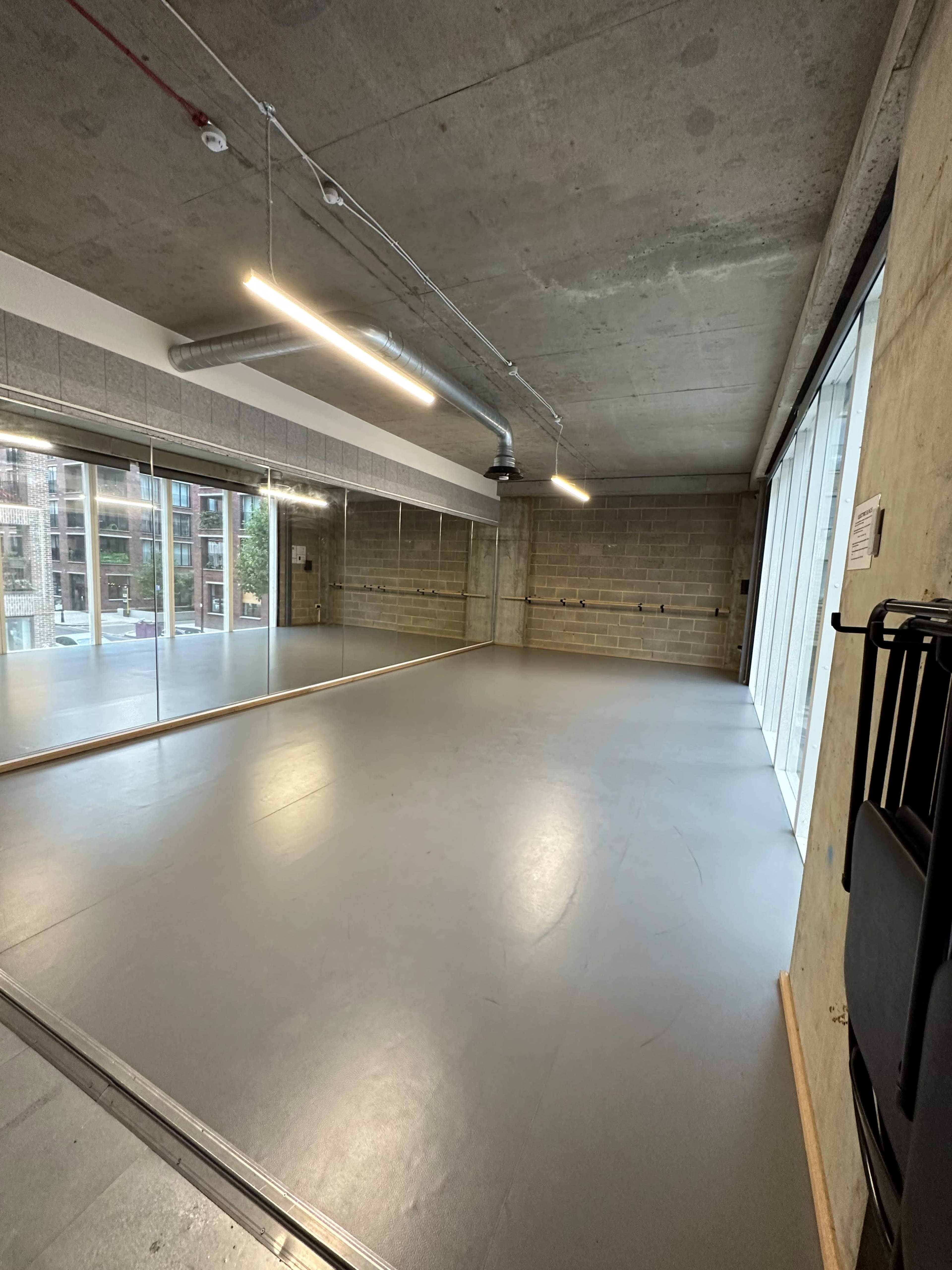 An empty studio space with a polished floor, large mirrors on one wall, and windows letting in natural light.