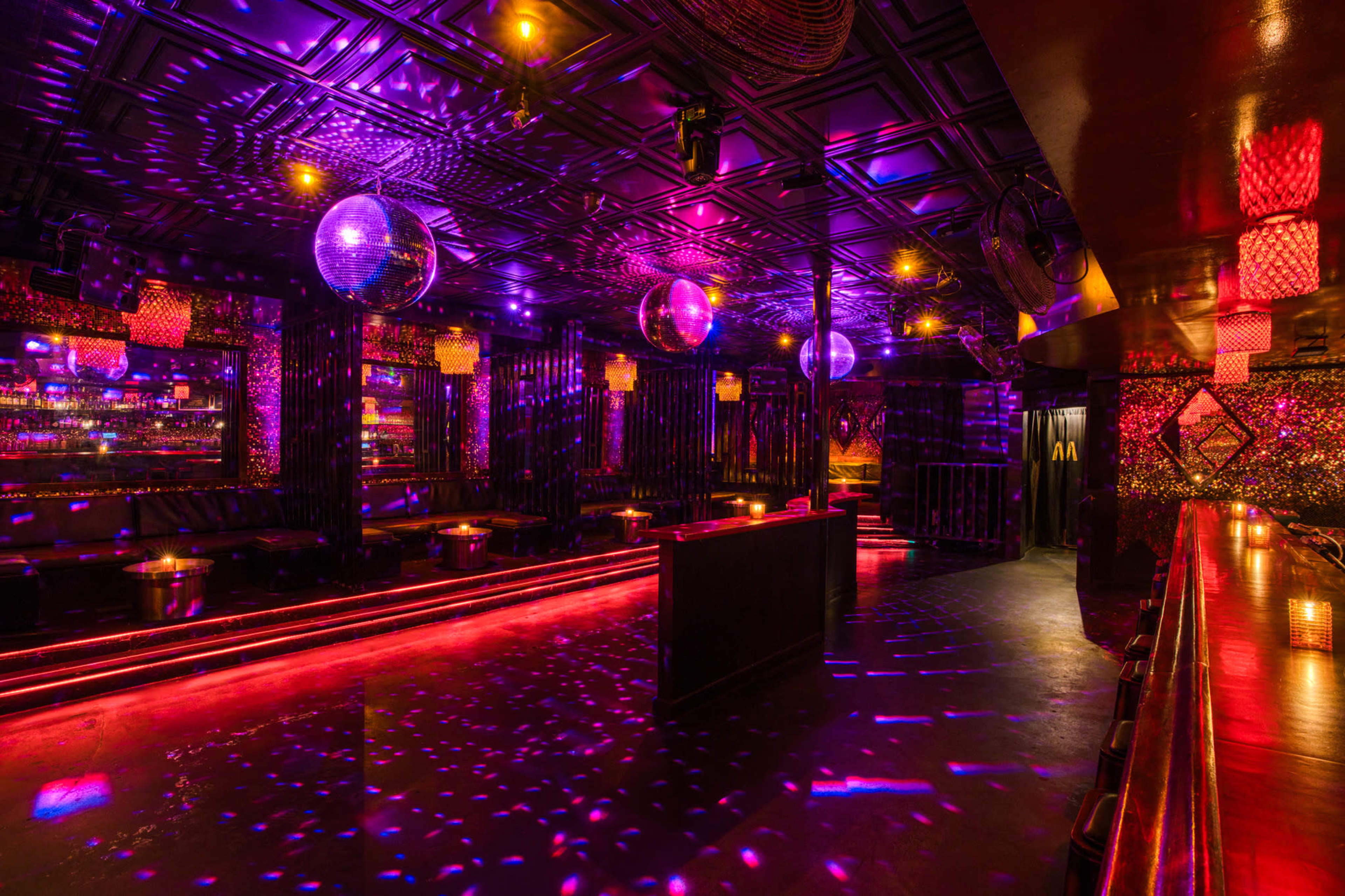 A dimly lit nightclub with colorful lights, disco balls, and a dance floor featuring reflections on the walls and ceiling.