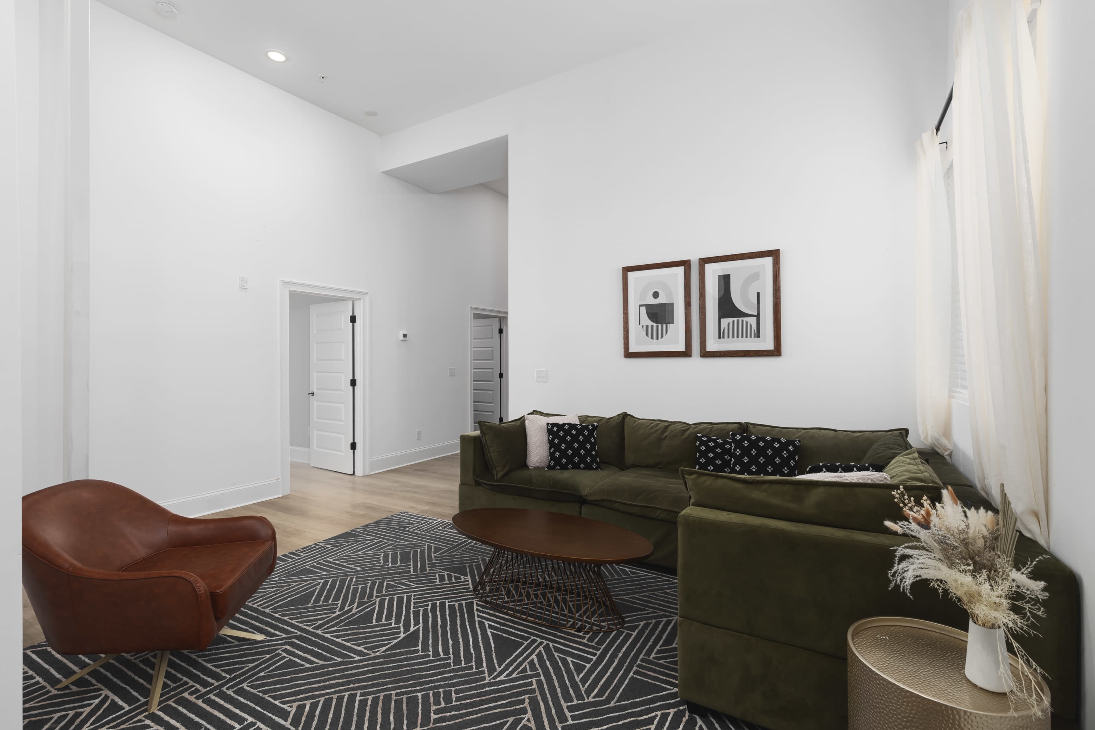 A modern living room features a green sofa, a brown accent chair, a round coffee table, and framed artwork on the walls.