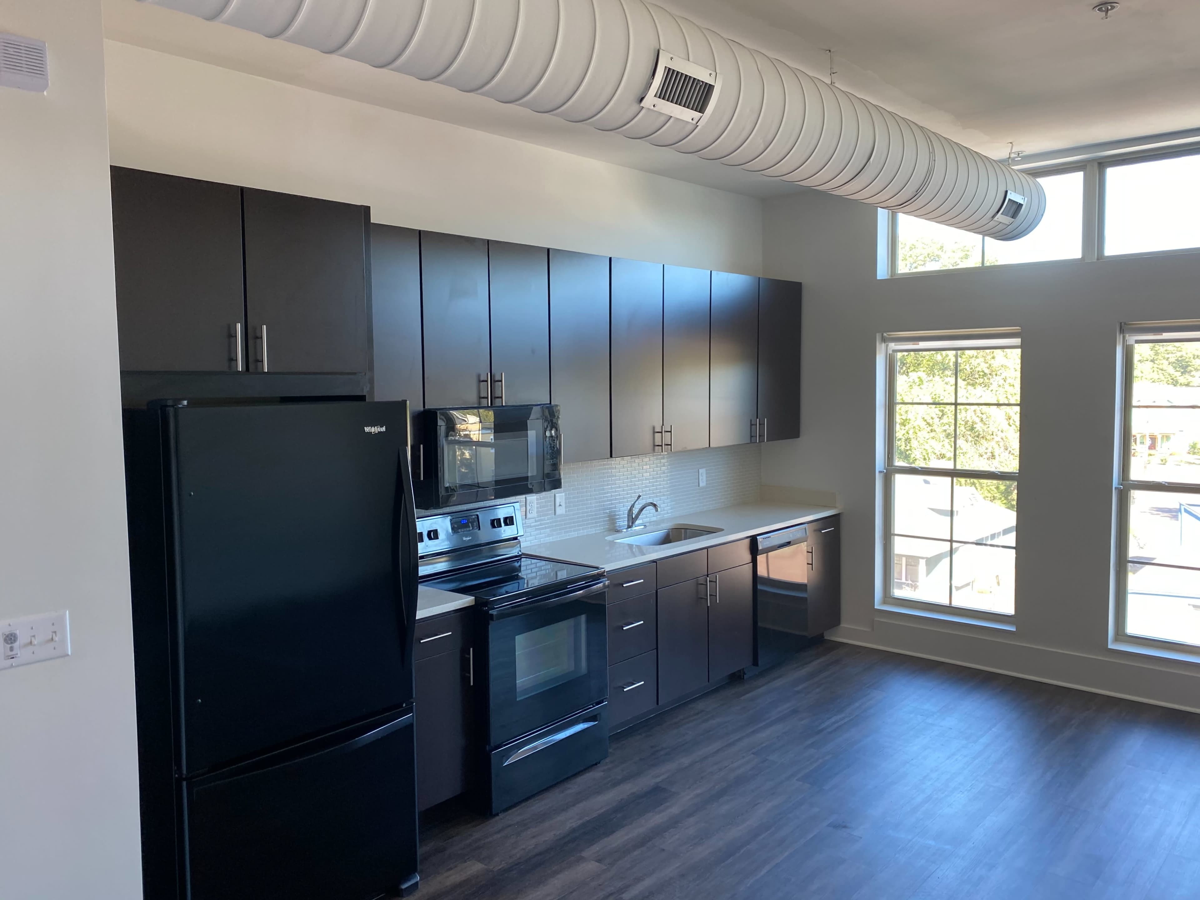 A modern kitchen with dark cabinets, stainless steel appliances, and large windows letting in natural light.