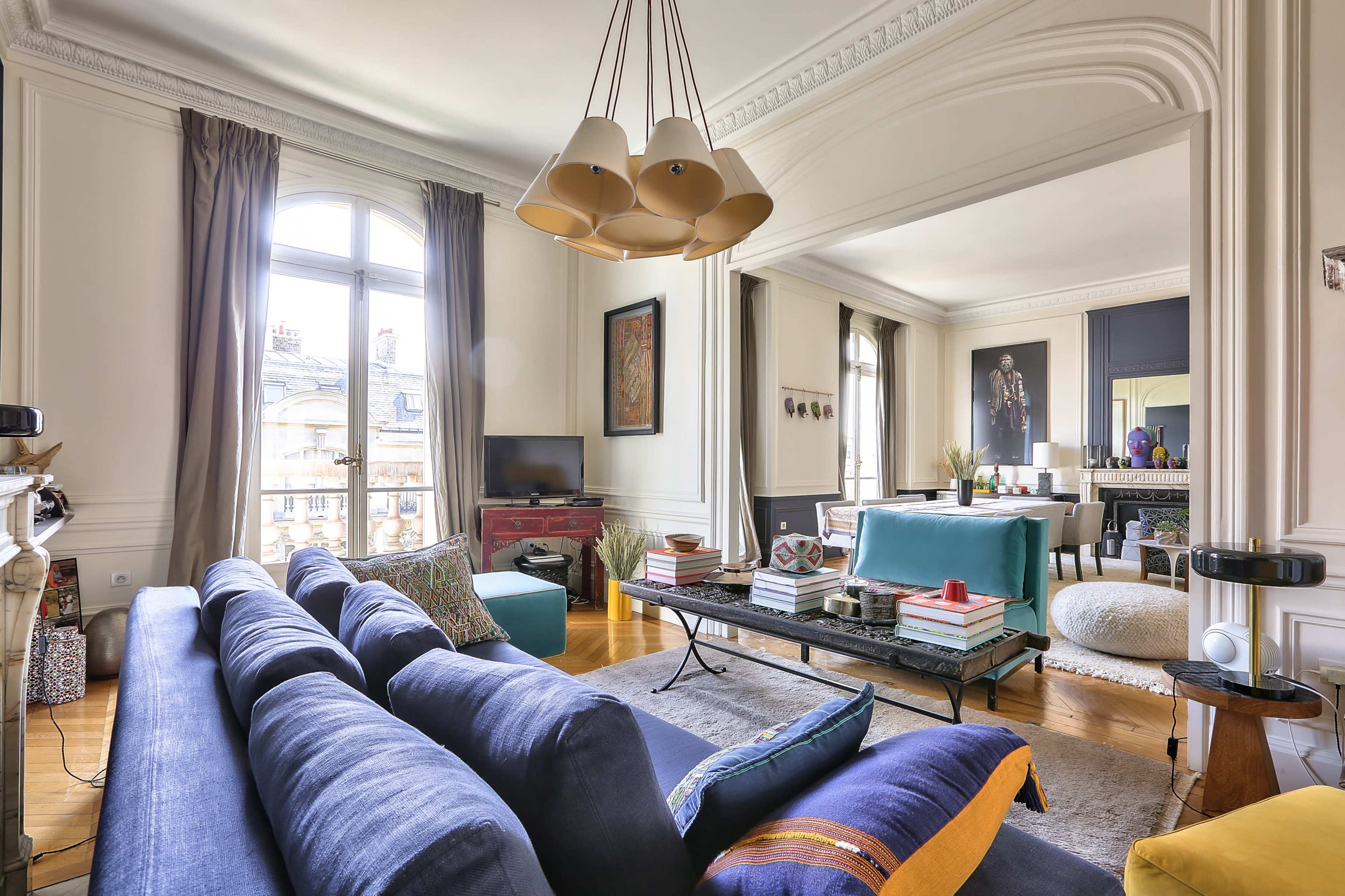 A modern living room features a blue sofa, a coffee table adorned with books and decor, and large windows allowing natural light to fill the space.