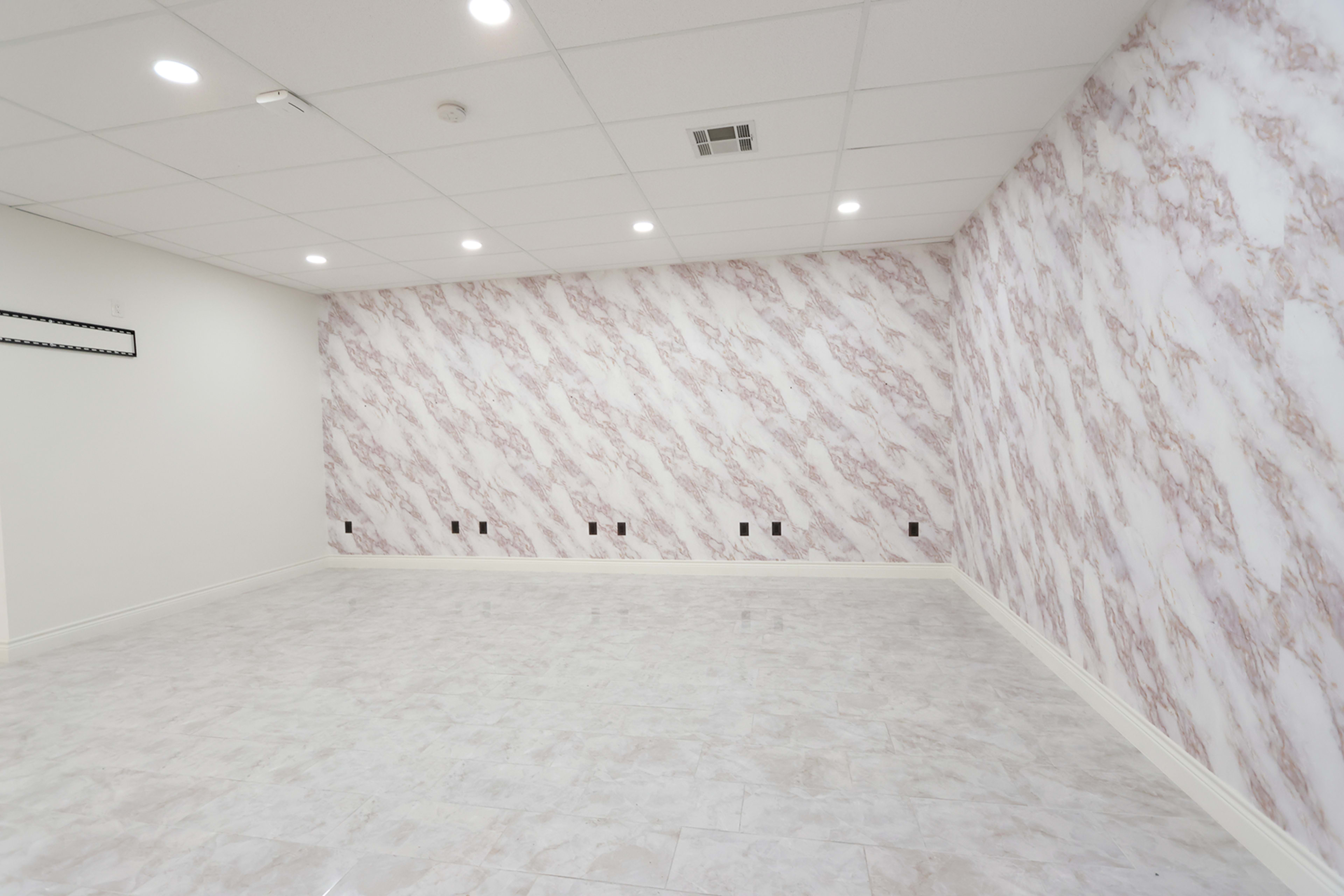 An empty room with a marble-patterned wall and tiled flooring, featuring multiple electrical outlets along the base.