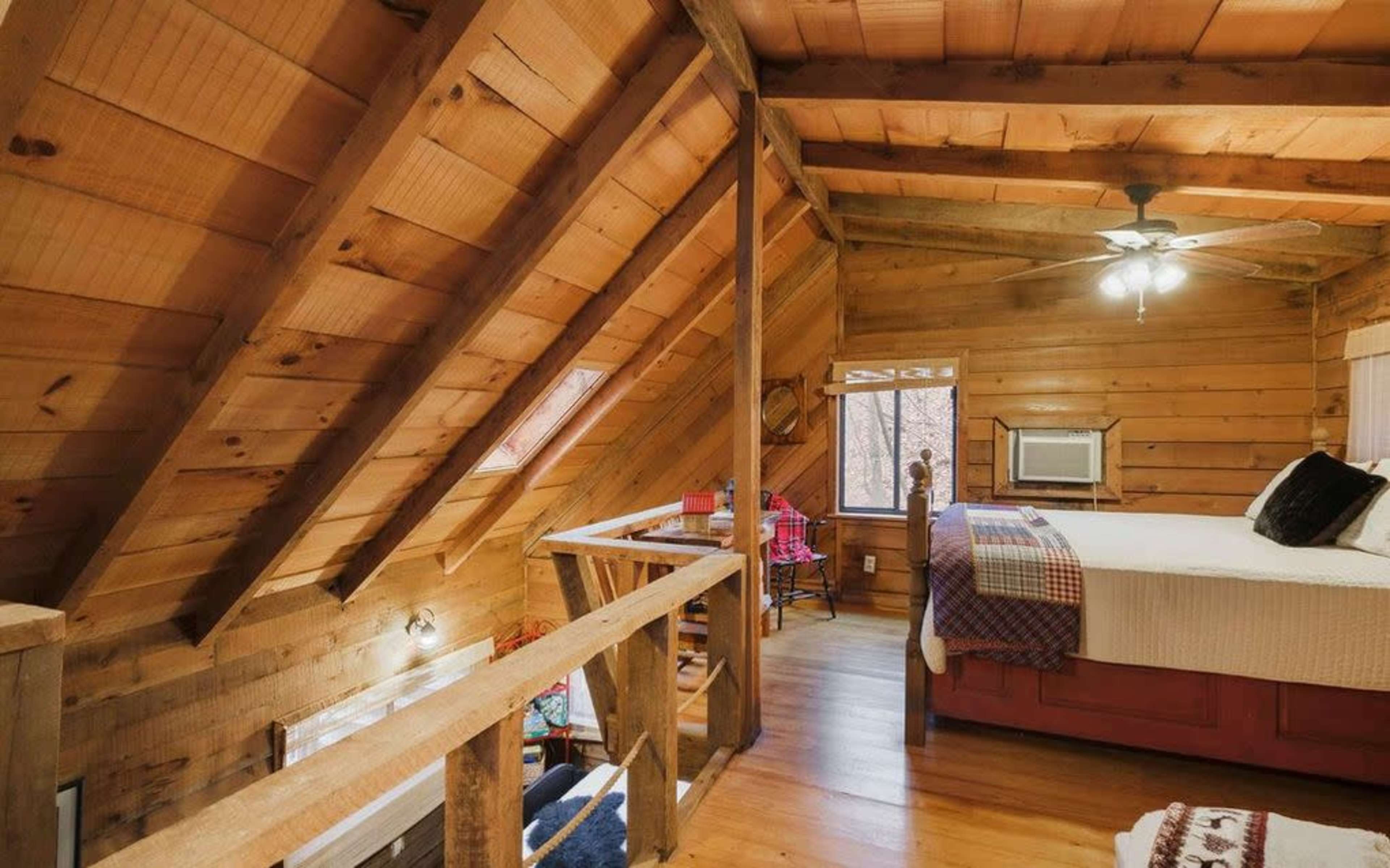 A wooden lofted bedroom with a sloped ceiling, featuring a bed and a small seating area with a table and chairs.