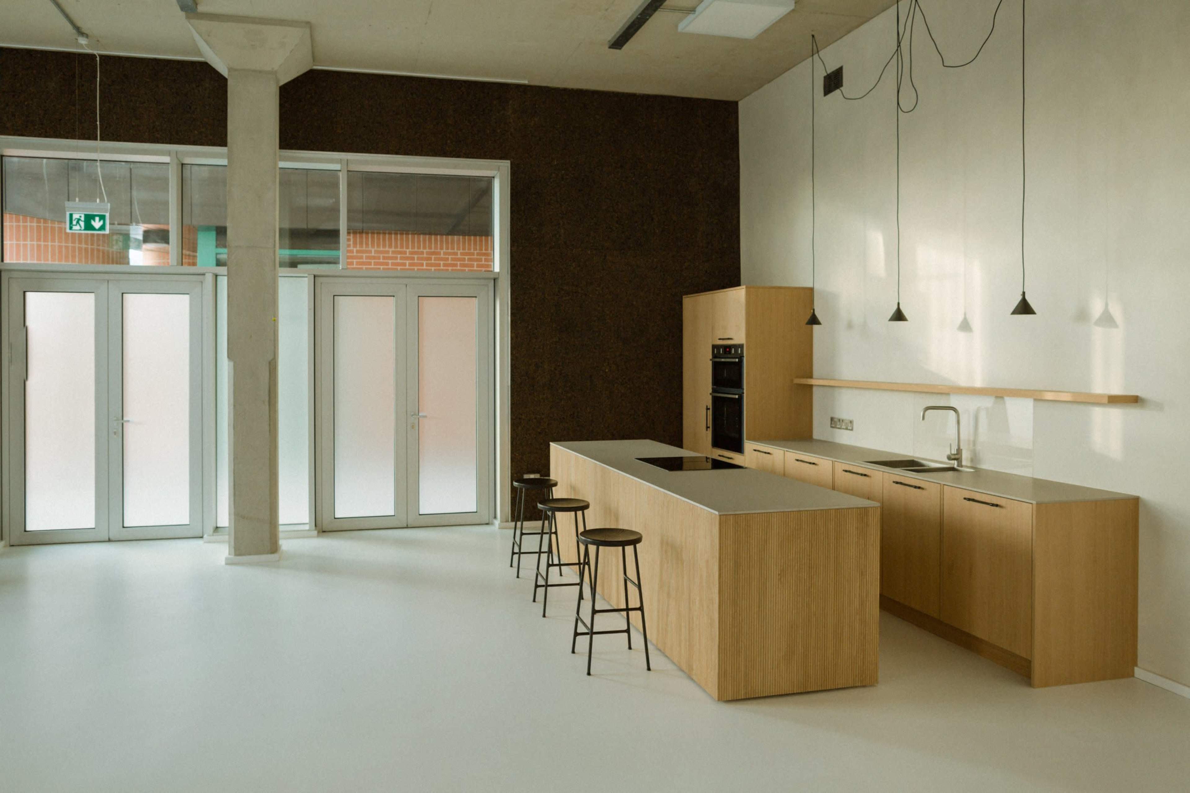 A modern kitchen with a wooden island, bar stools, and minimalistic cabinetry in a spacious, well-lit area.