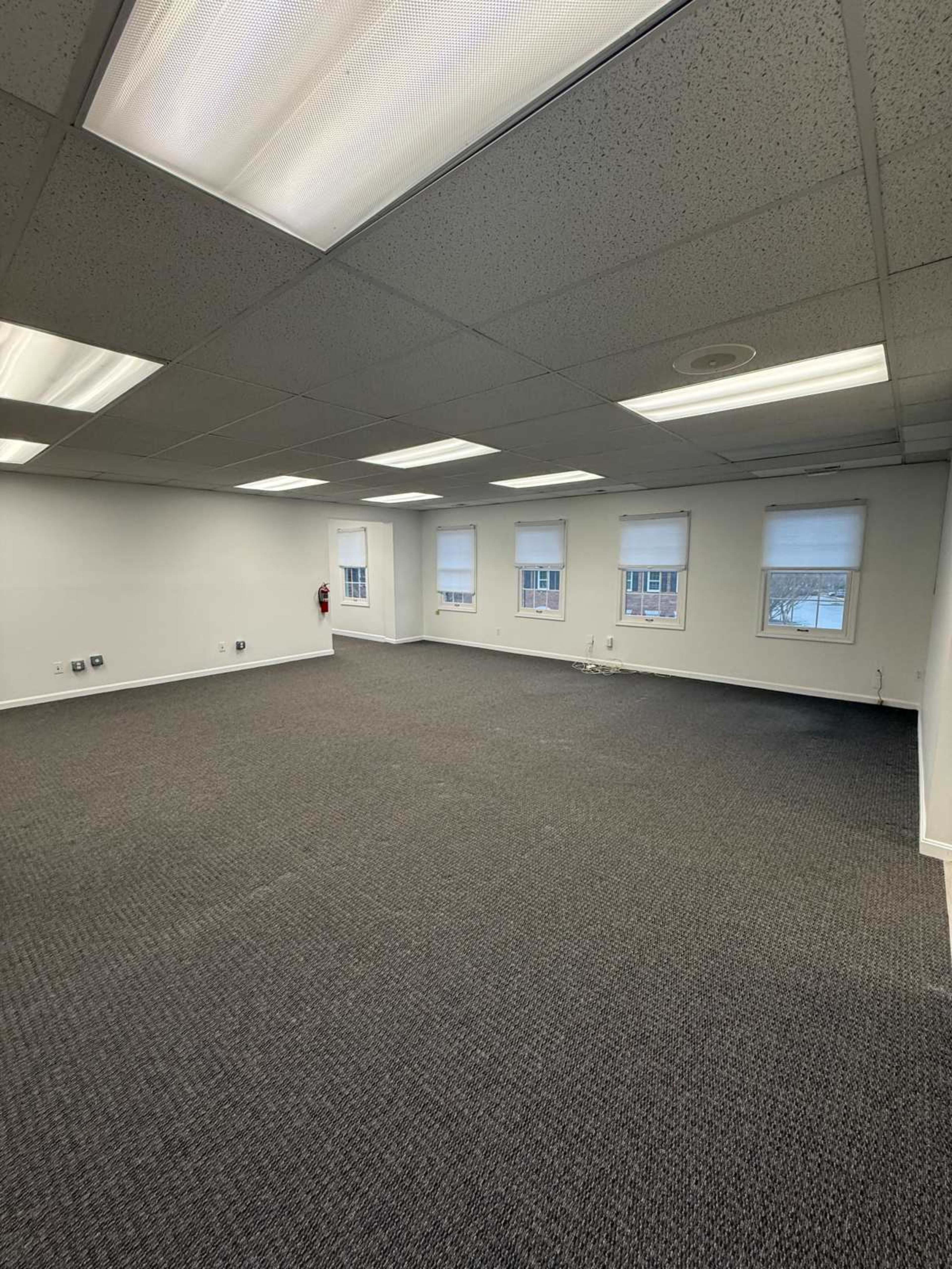An empty office space features carpeted flooring and several windows with light blinds.