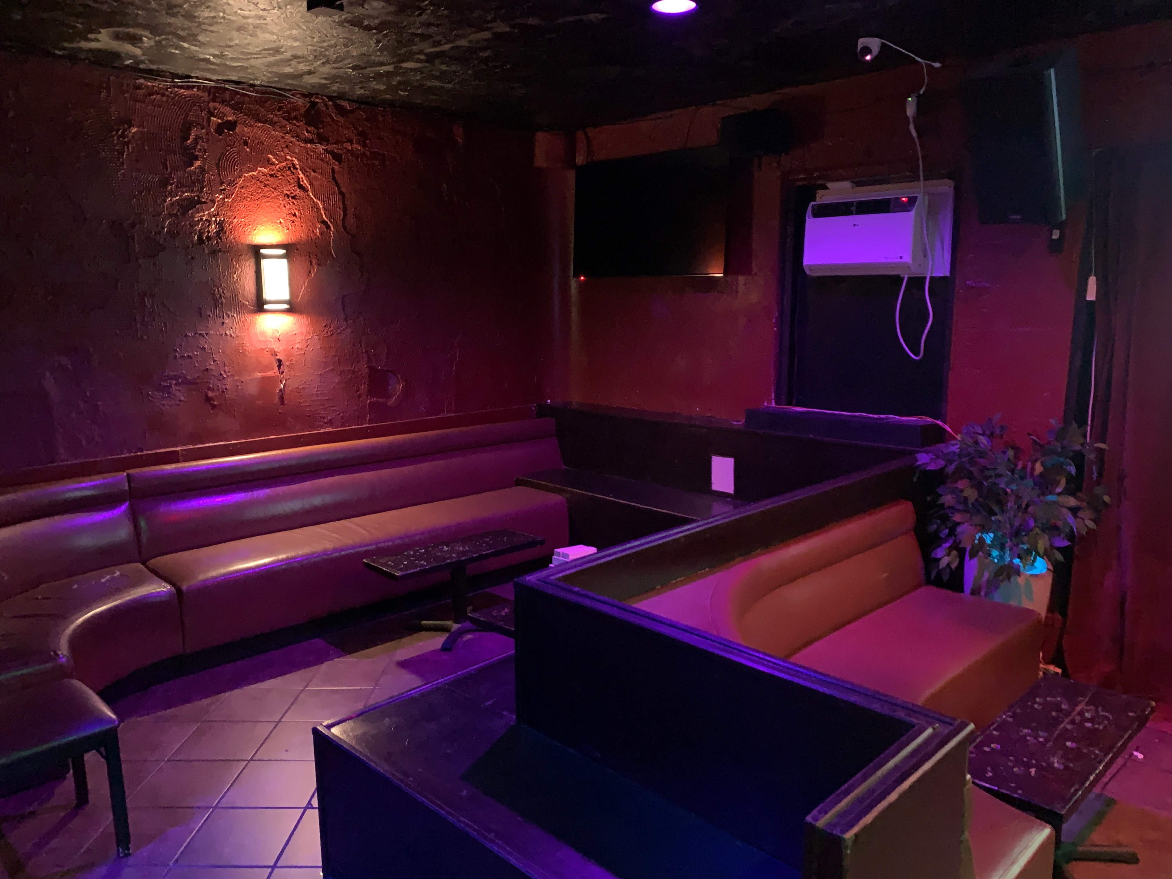 A dimly lit lounge area with dark red walls, several seating arrangements, and an air conditioning unit on the wall.