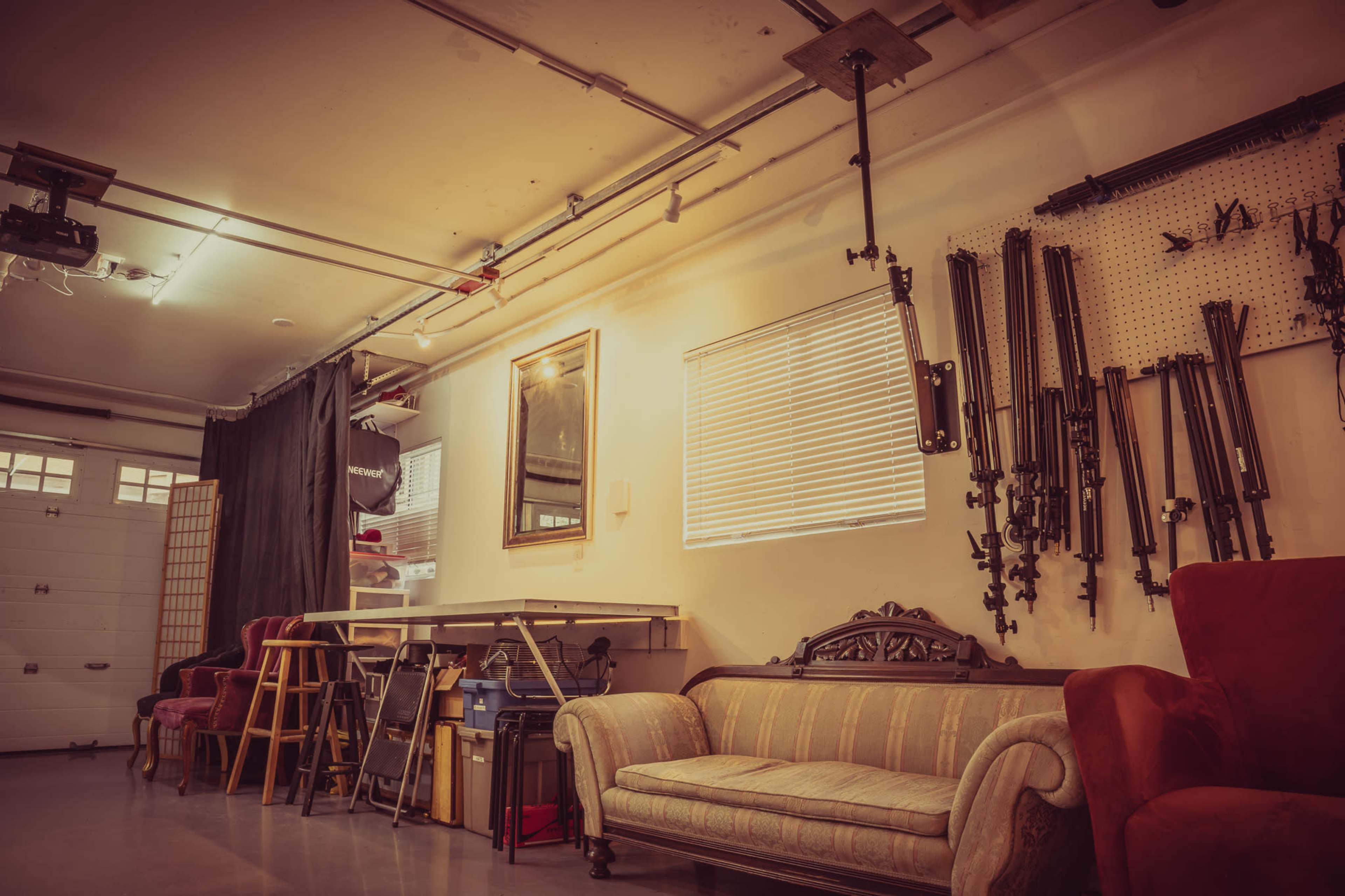 A garage interior features a wooden table, various chairs, a couch, and several tools mounted on the wall.
