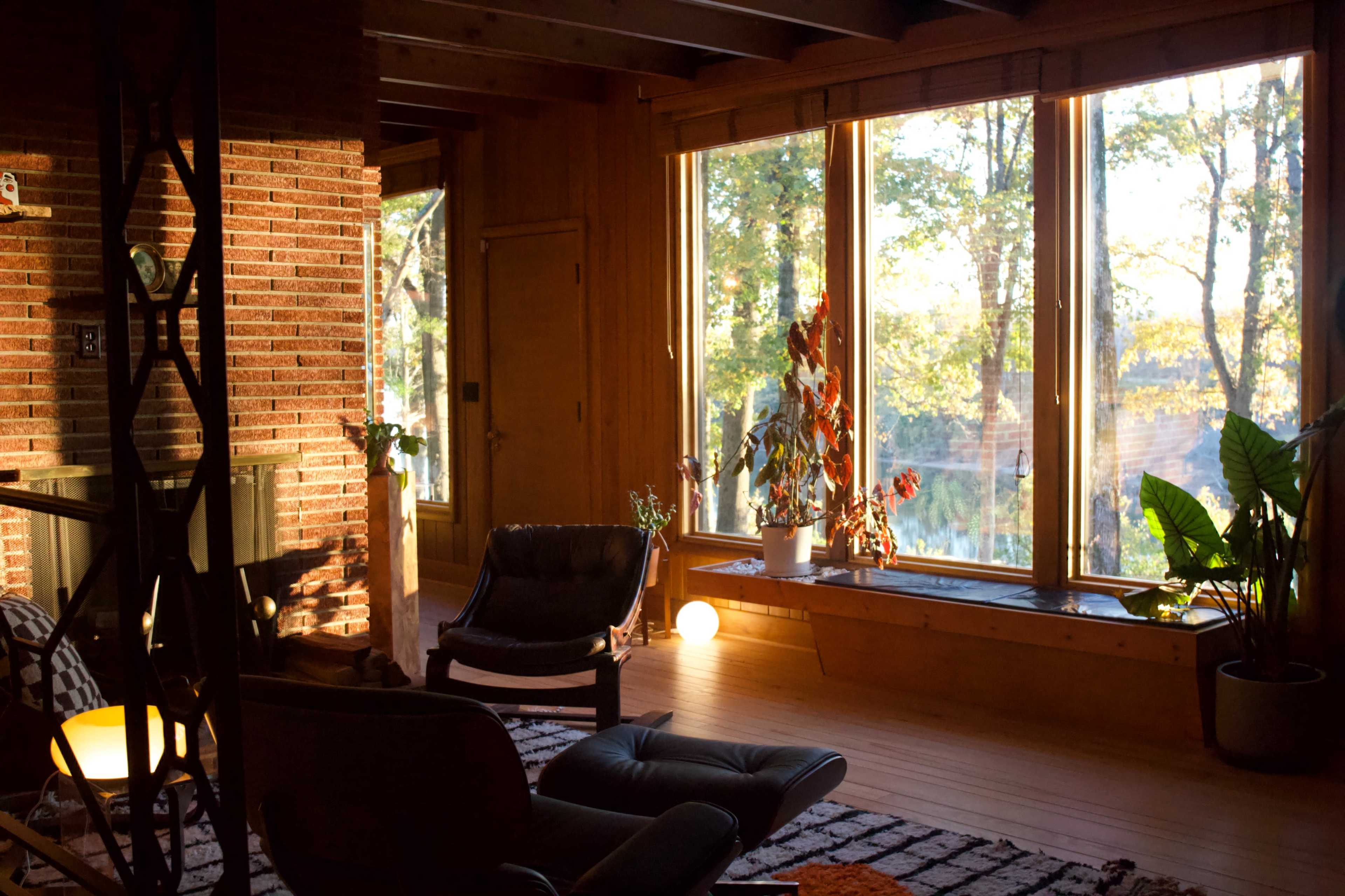 The room features large windows with natural light streaming in, highlighting a cozy seating area with a fireplace and plants.
