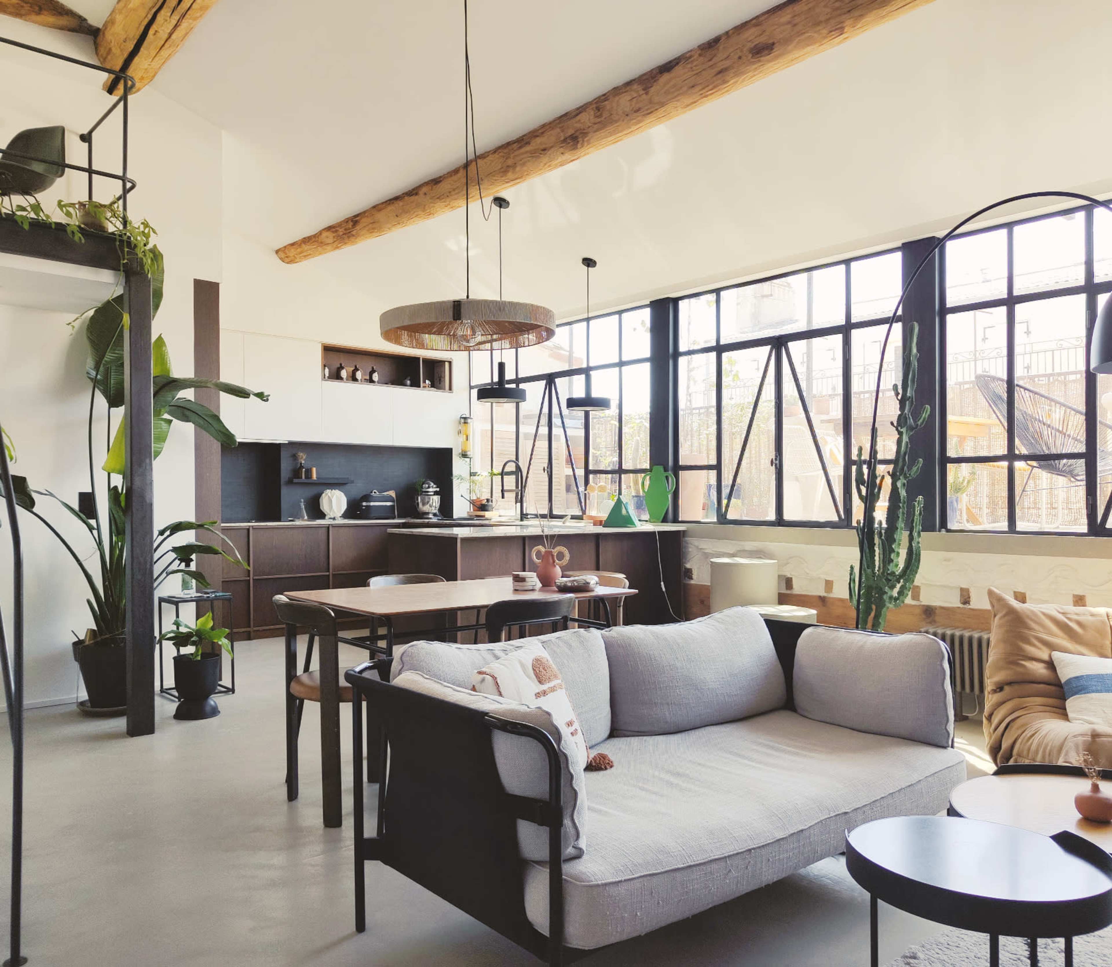 The image shows a modern, open-plan living area with a sofa, dining table, and large windows allowing natural light to flow in.