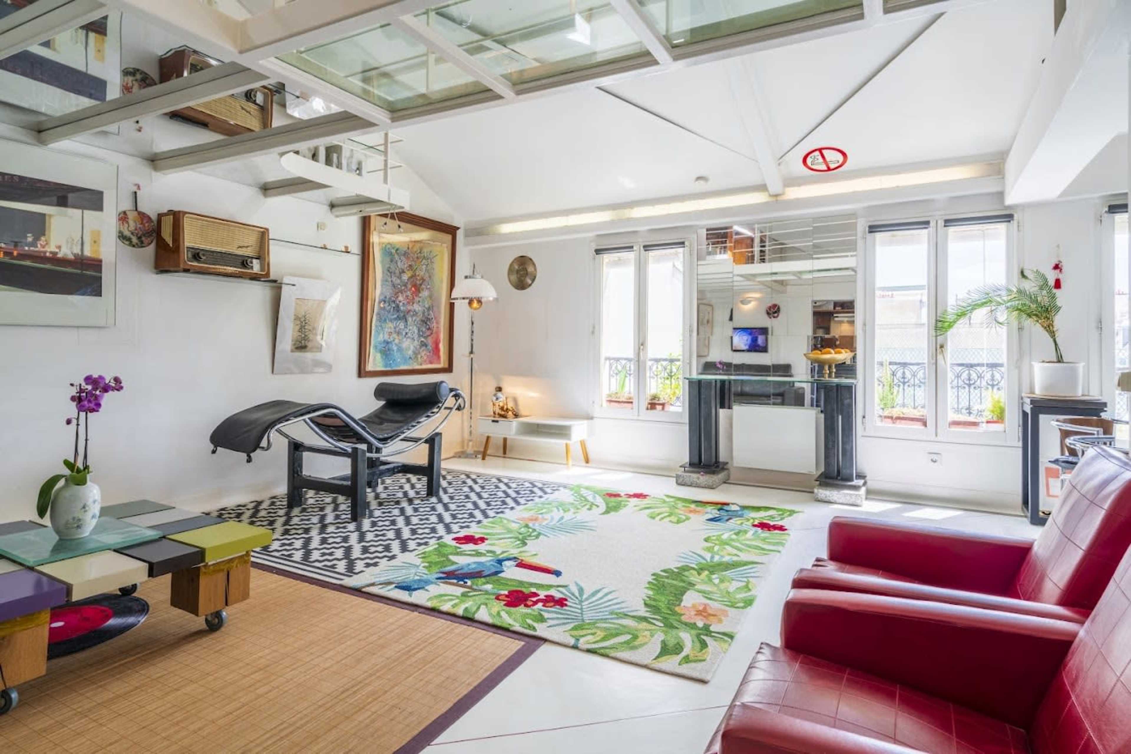 The image shows a modern living room with a colorful rug, a red leather sofa, and various decorative items, including a vintage radio and artwork on the walls.