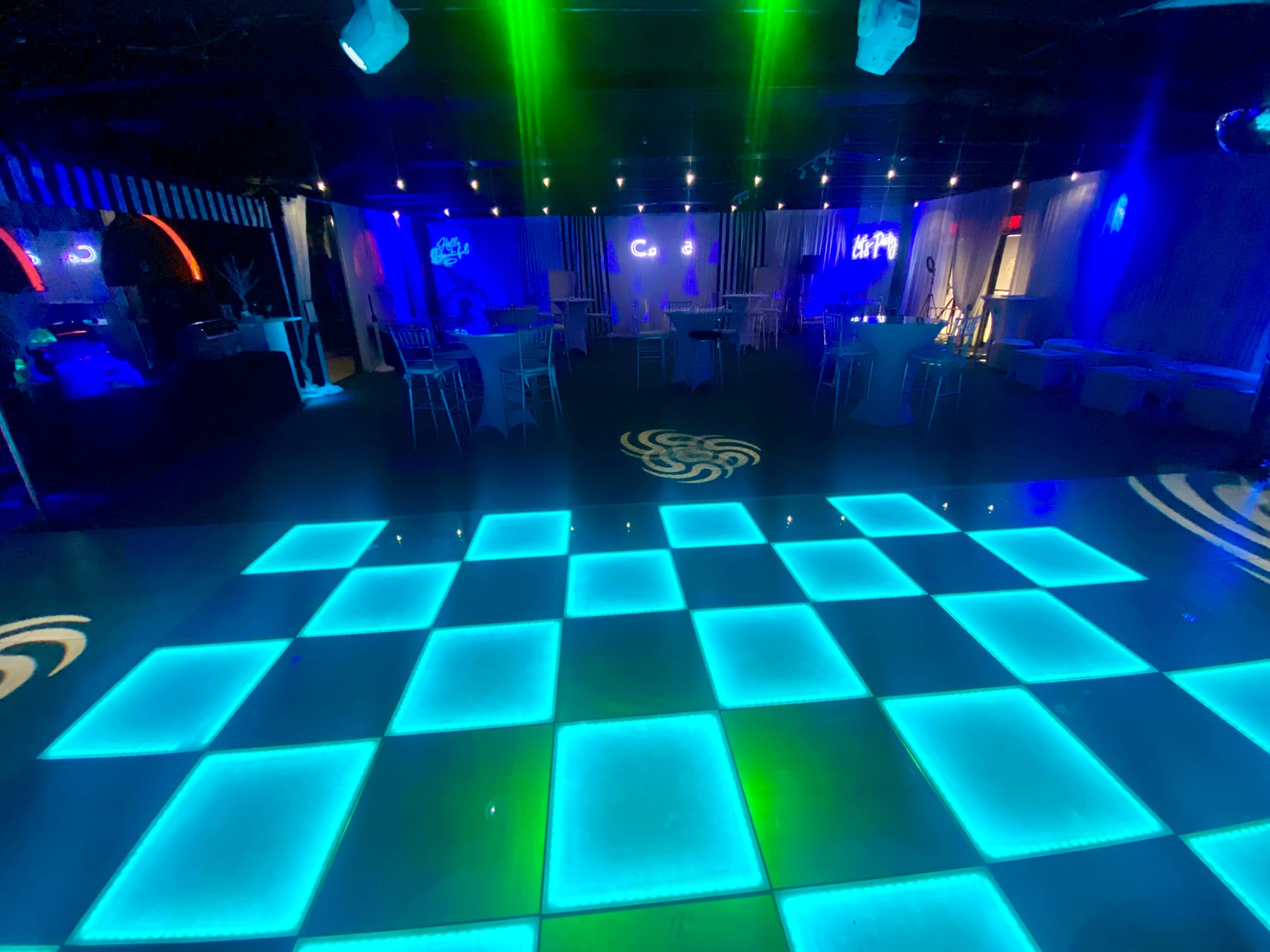 The image shows a dimly lit dance floor with illuminated blue square tiles and colorful lights in a nightclub setting.