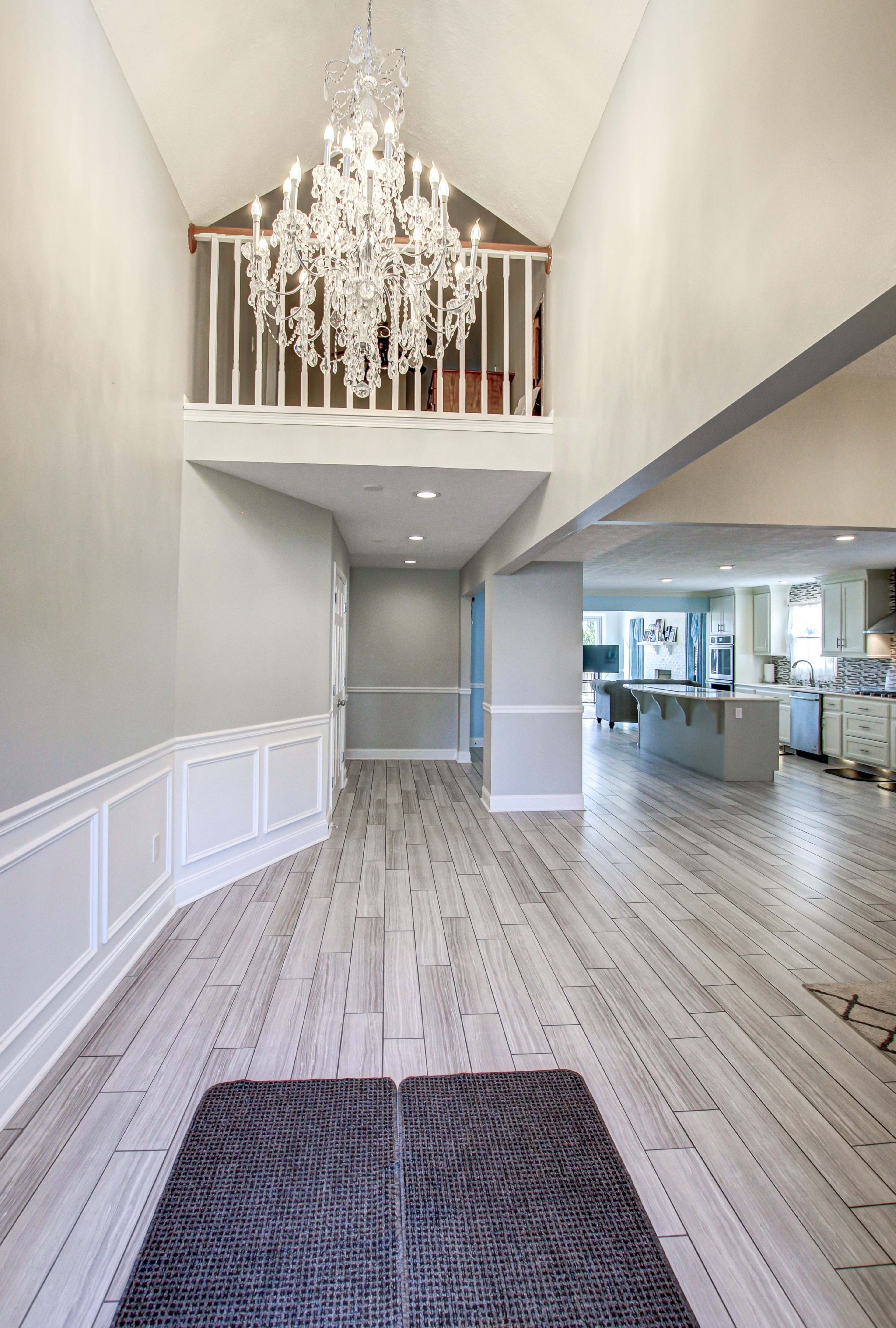 A spacious foyer with a tall ceiling, a chandelier, and a view of a kitchen in the background.