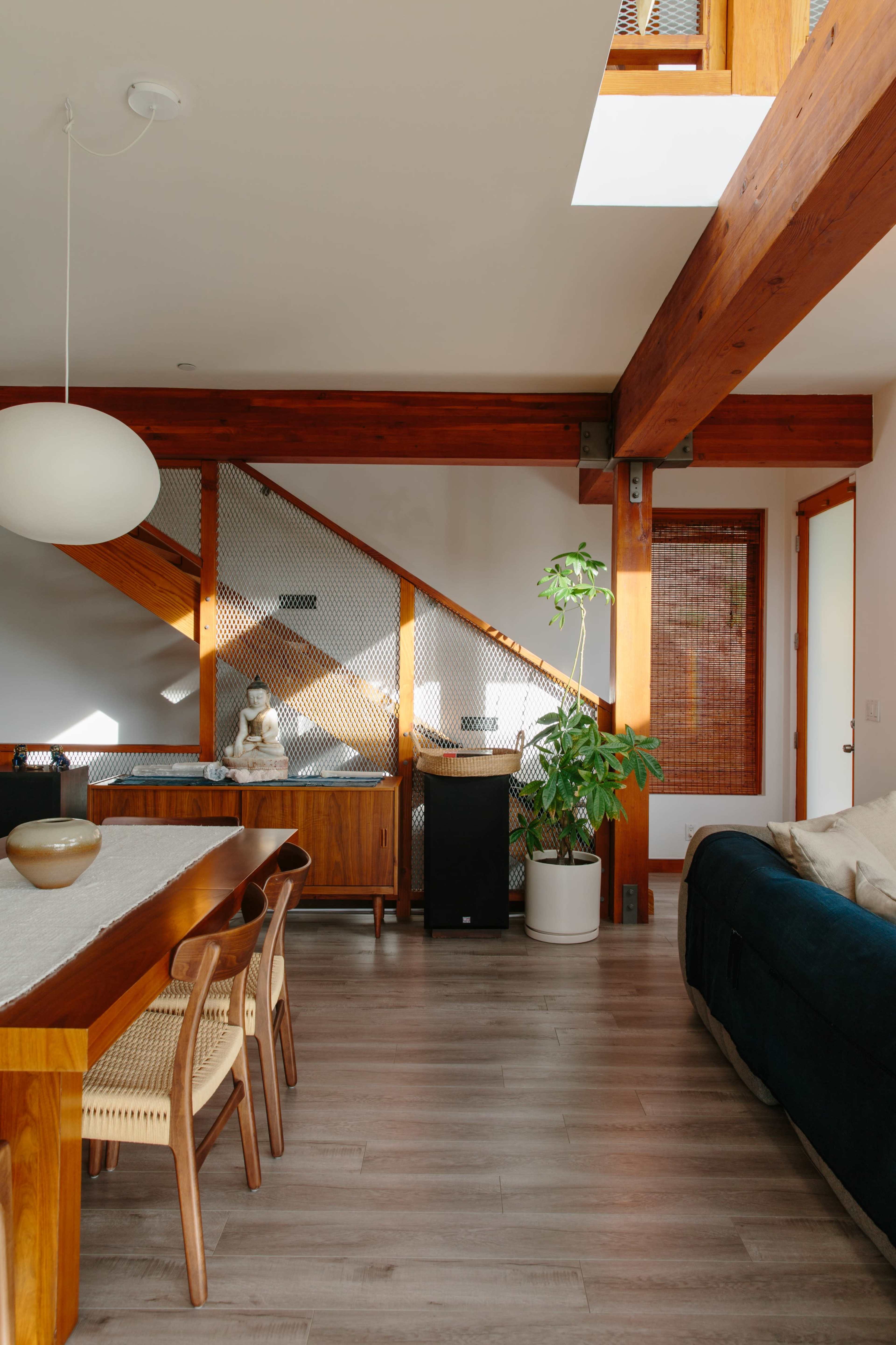 A contemporary living space featuring a wooden dining table with chairs, a staircase with a decorative railing, and a potted plant in a corner.