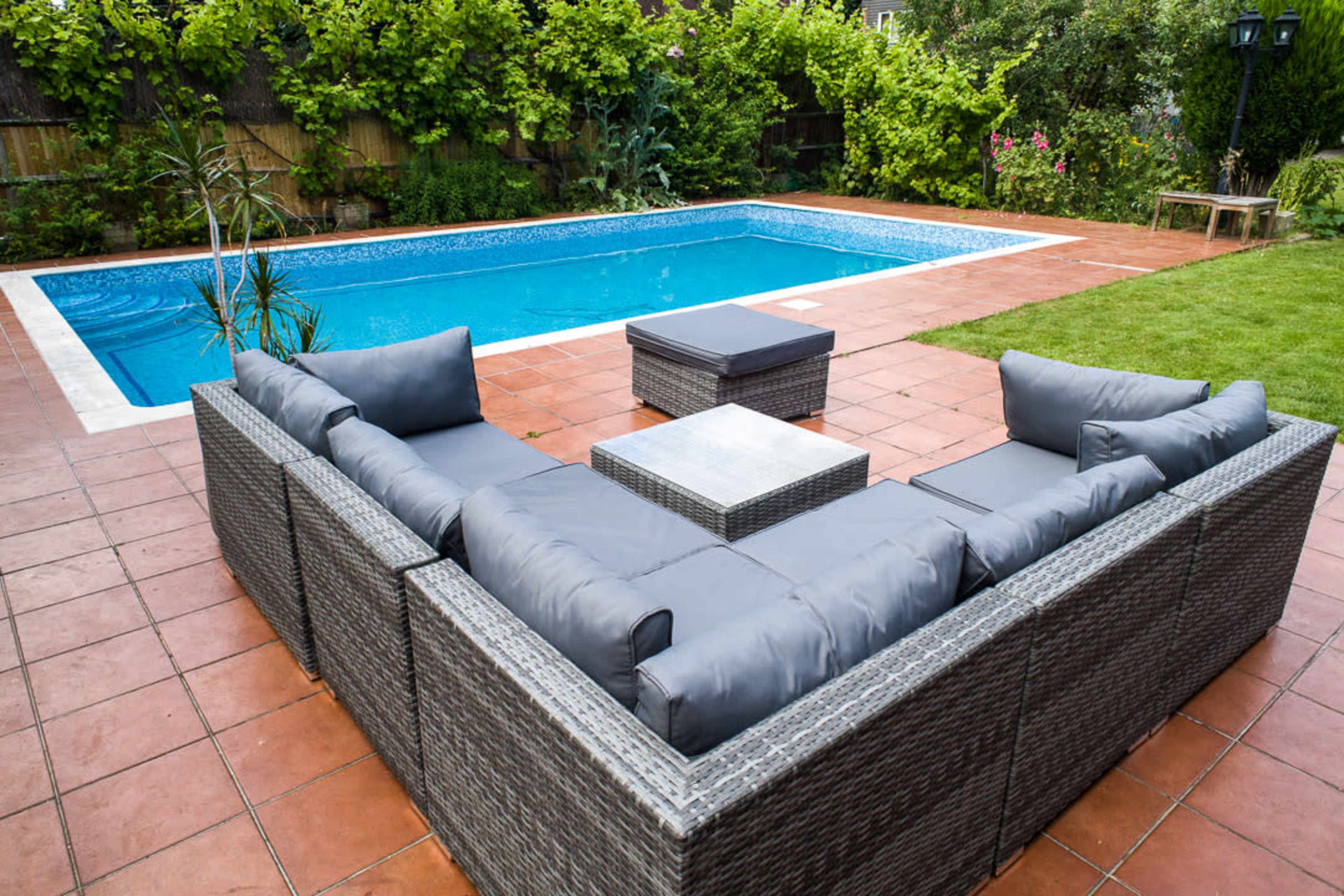 A patio area with a rectangular swimming pool surrounded by tile flooring and a seating arrangement made of outdoor furniture.
