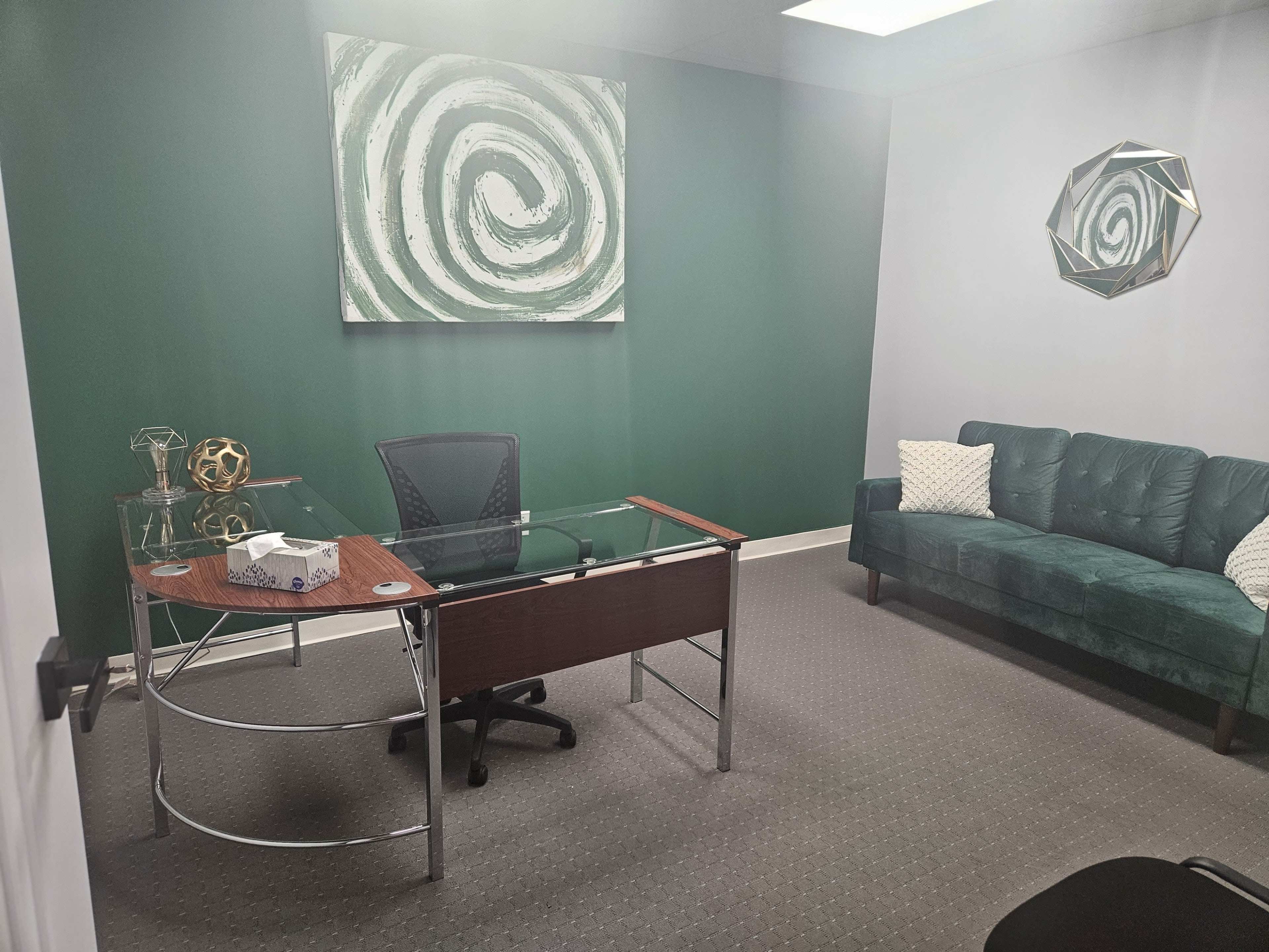 A modern office space featuring a glass-topped desk, a green sofa, and abstract wall art.