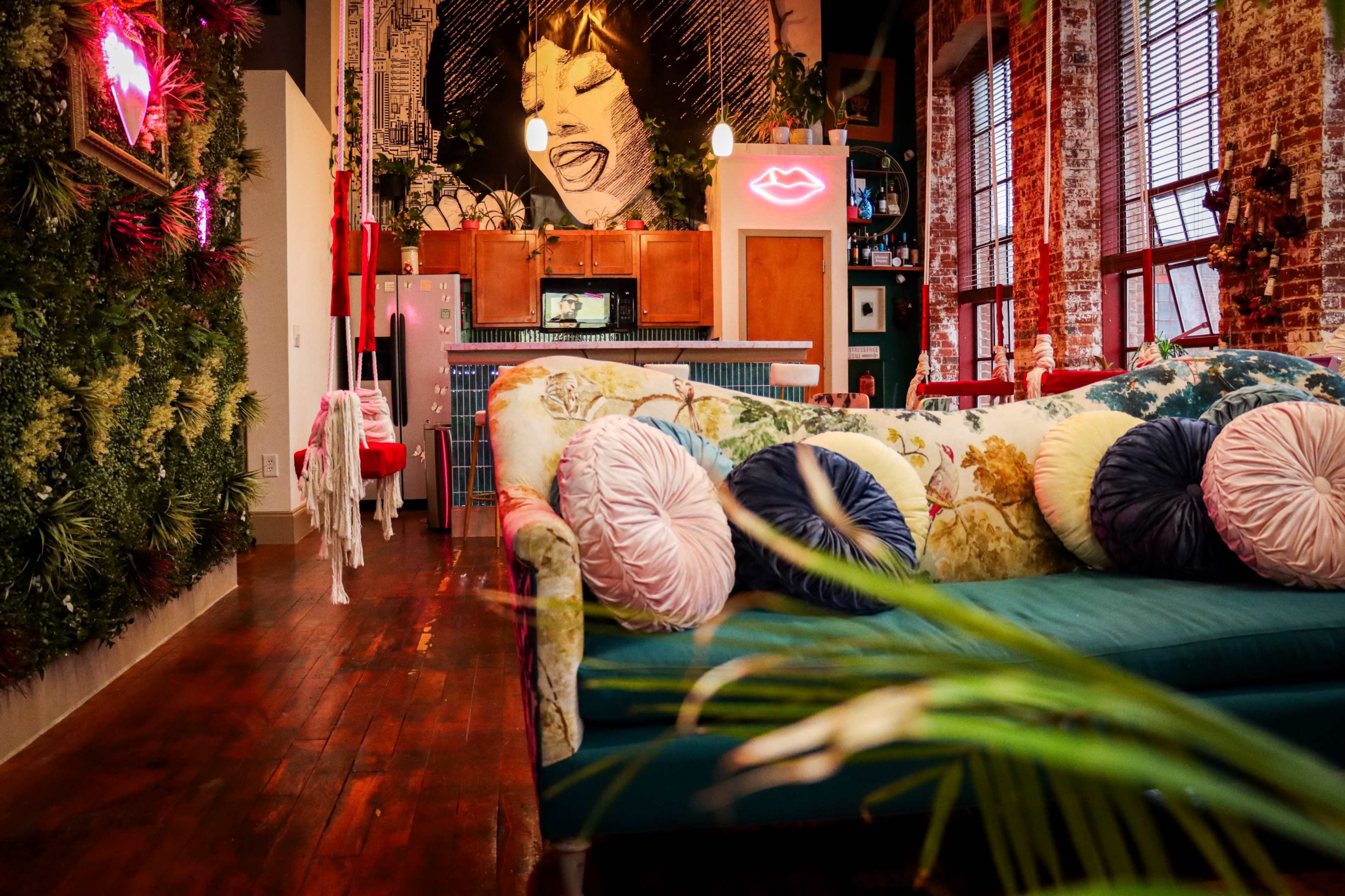 A vibrant, eclectic living space featuring a colorful sofa, lush greenery on the walls, and a large mural of a face in the background.