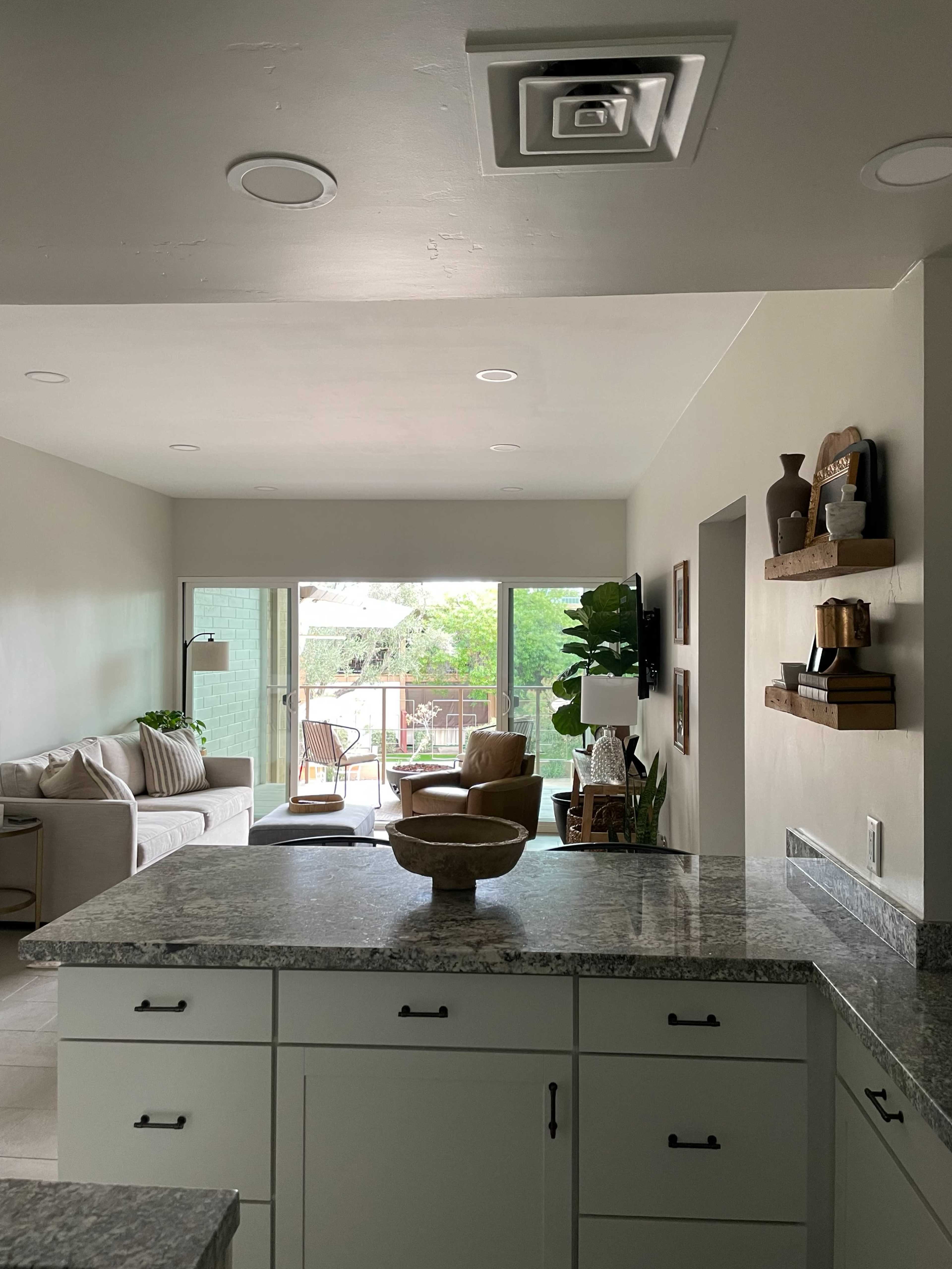 A kitchen area with a granite countertop, cabinets, and a view through large windows to an outdoor space with seating.