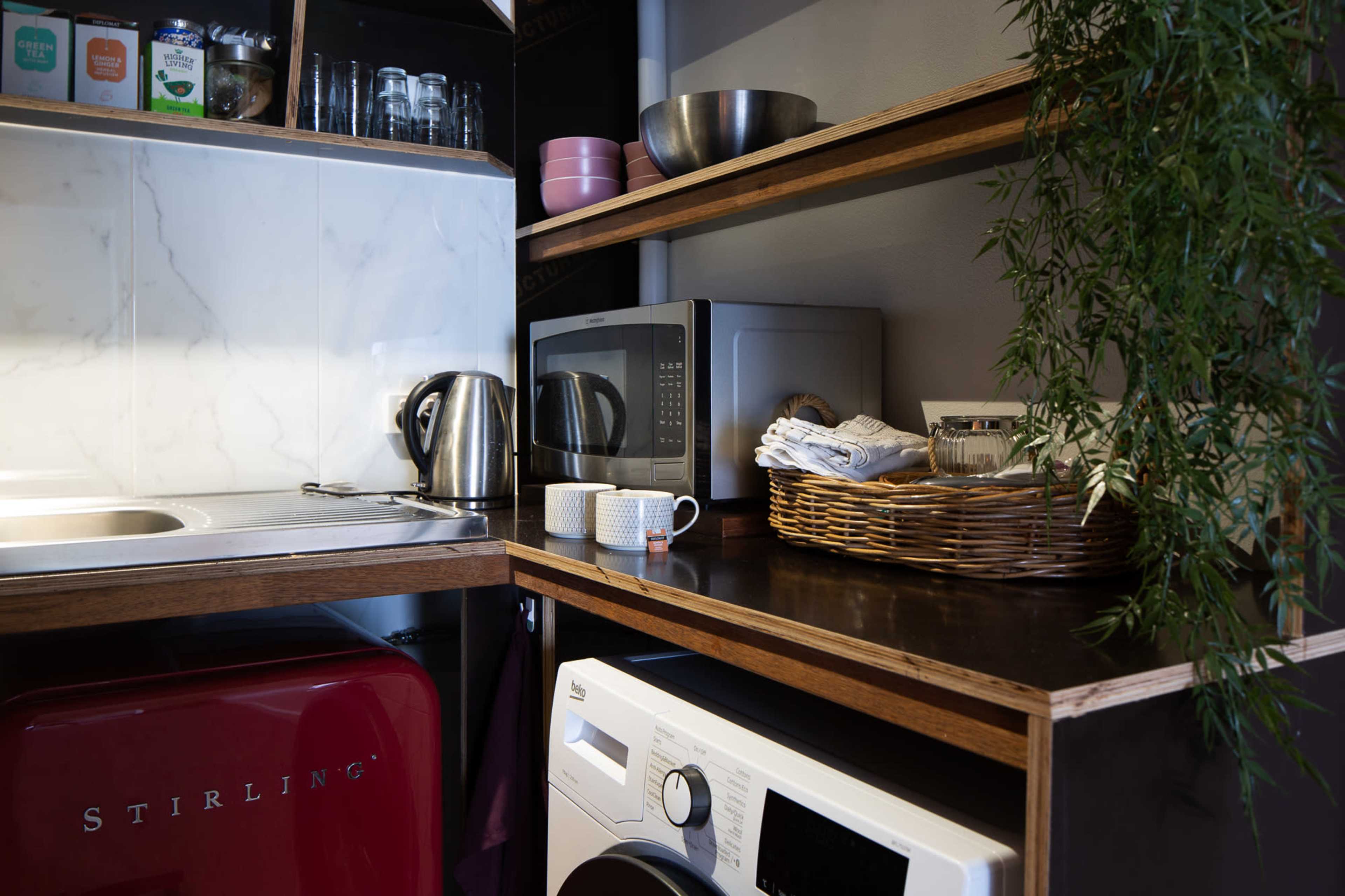A compact kitchen area with a red refrigerator, a microwave, and shelves containing kitchenware and a kettle.