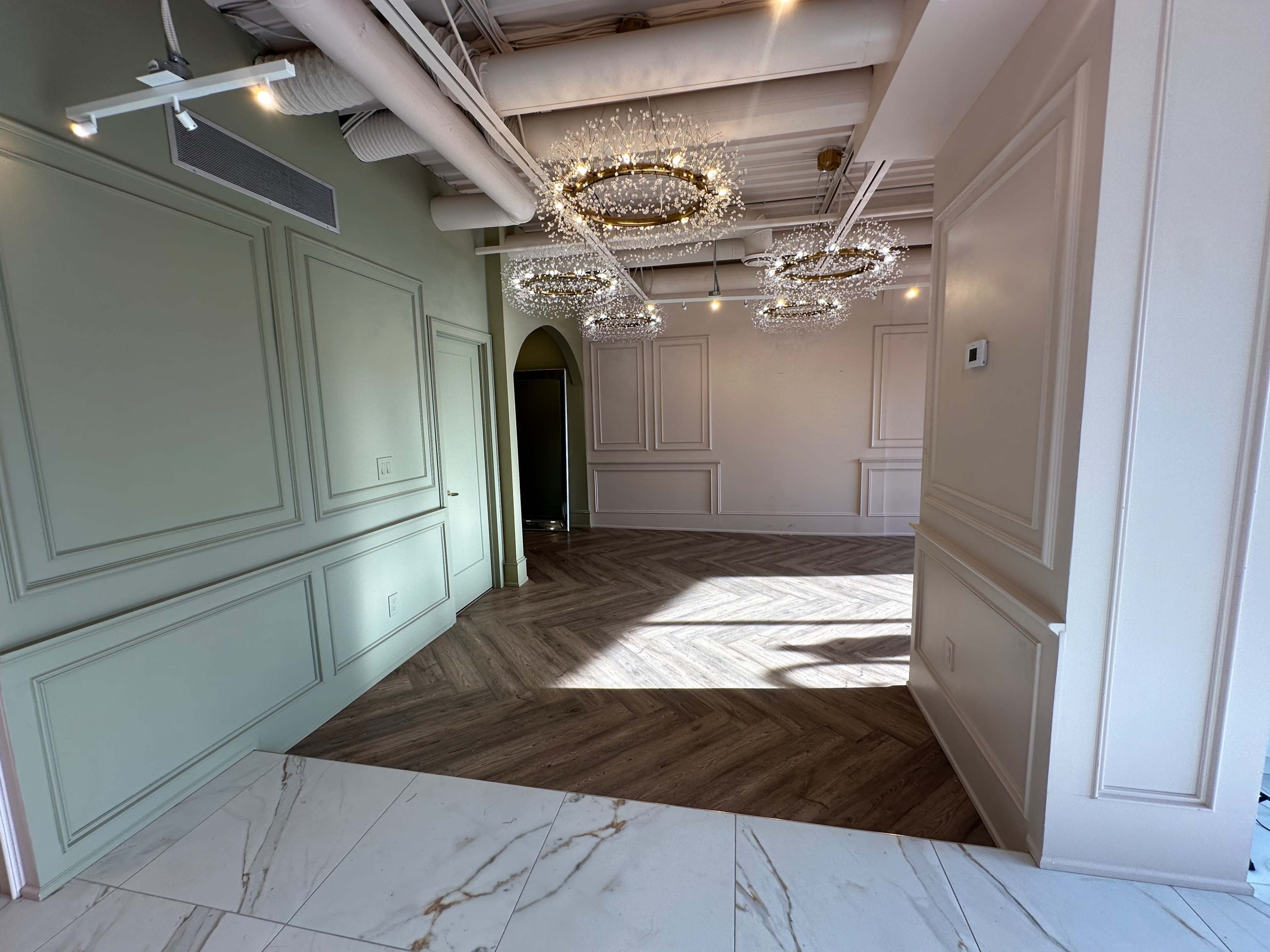 A spacious interior with decorative paneling, wooden flooring in a herringbone pattern, and multiple hanging chandeliers.
