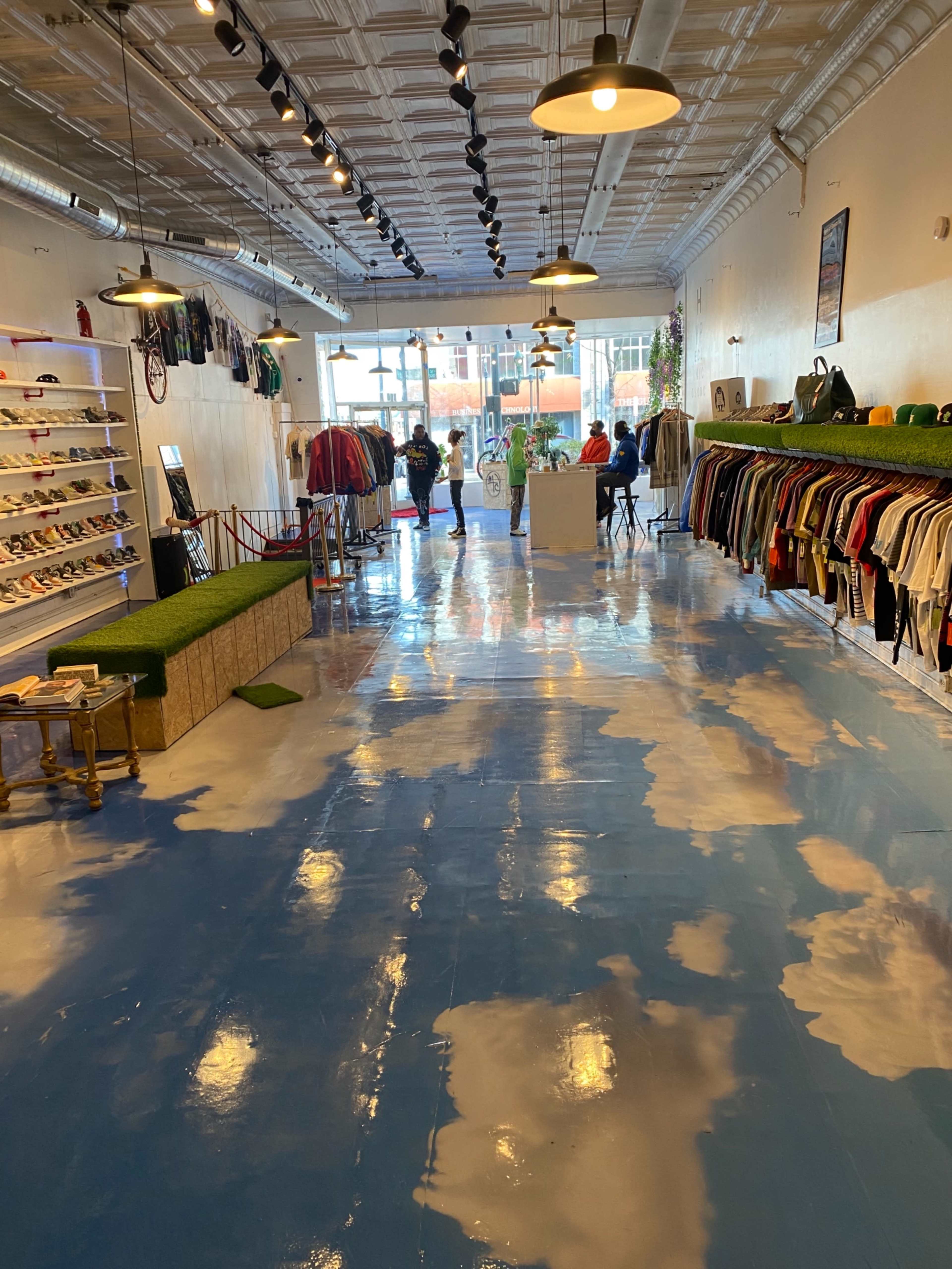 The interior of a retail store features a blue floor painted with cloud patterns, clothing racks along the walls, and customers browsing in the background.