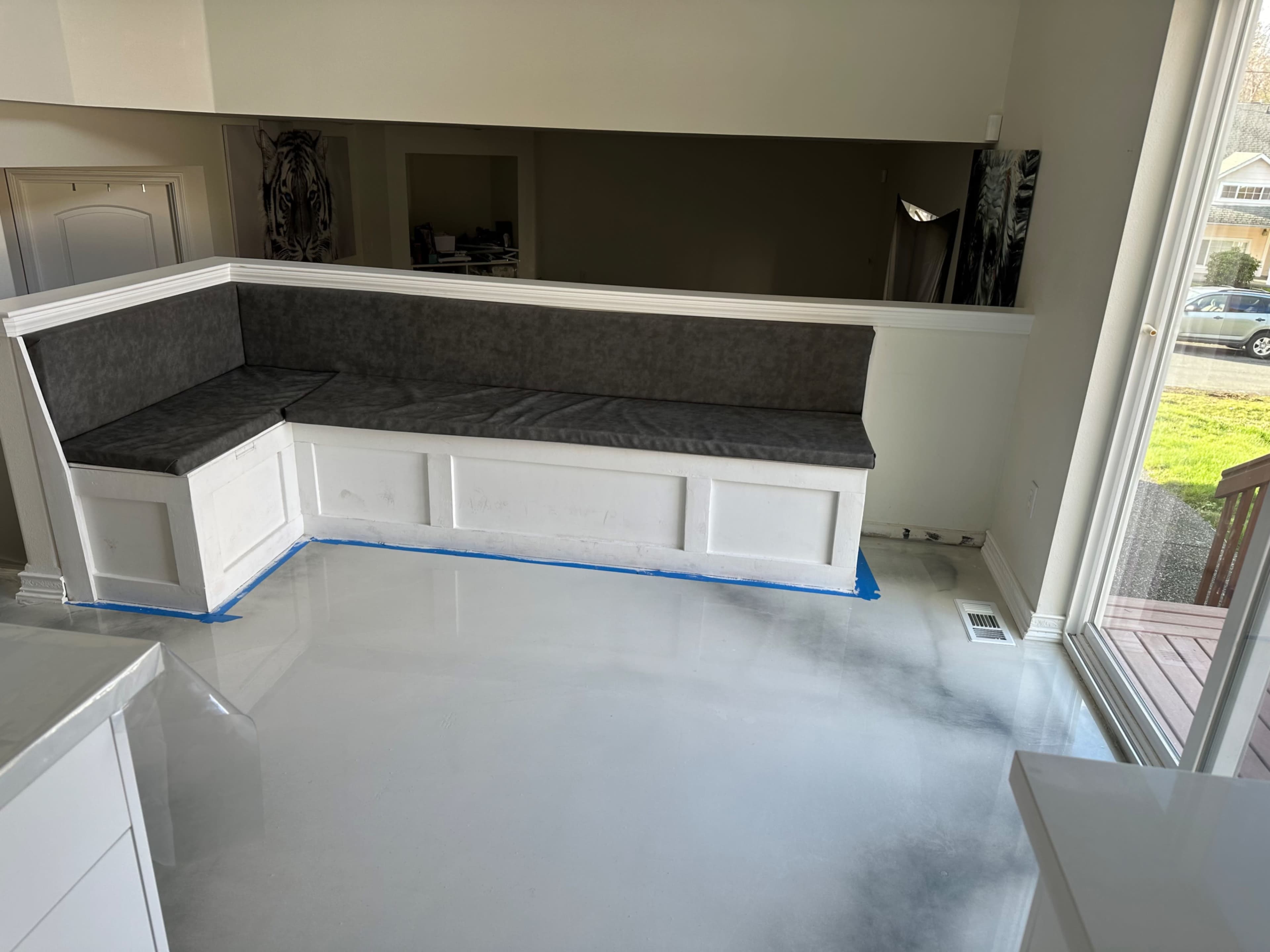 A partially renovated room with a gray cushioned bench built into a white panel along the wall, and a polished concrete floor.
