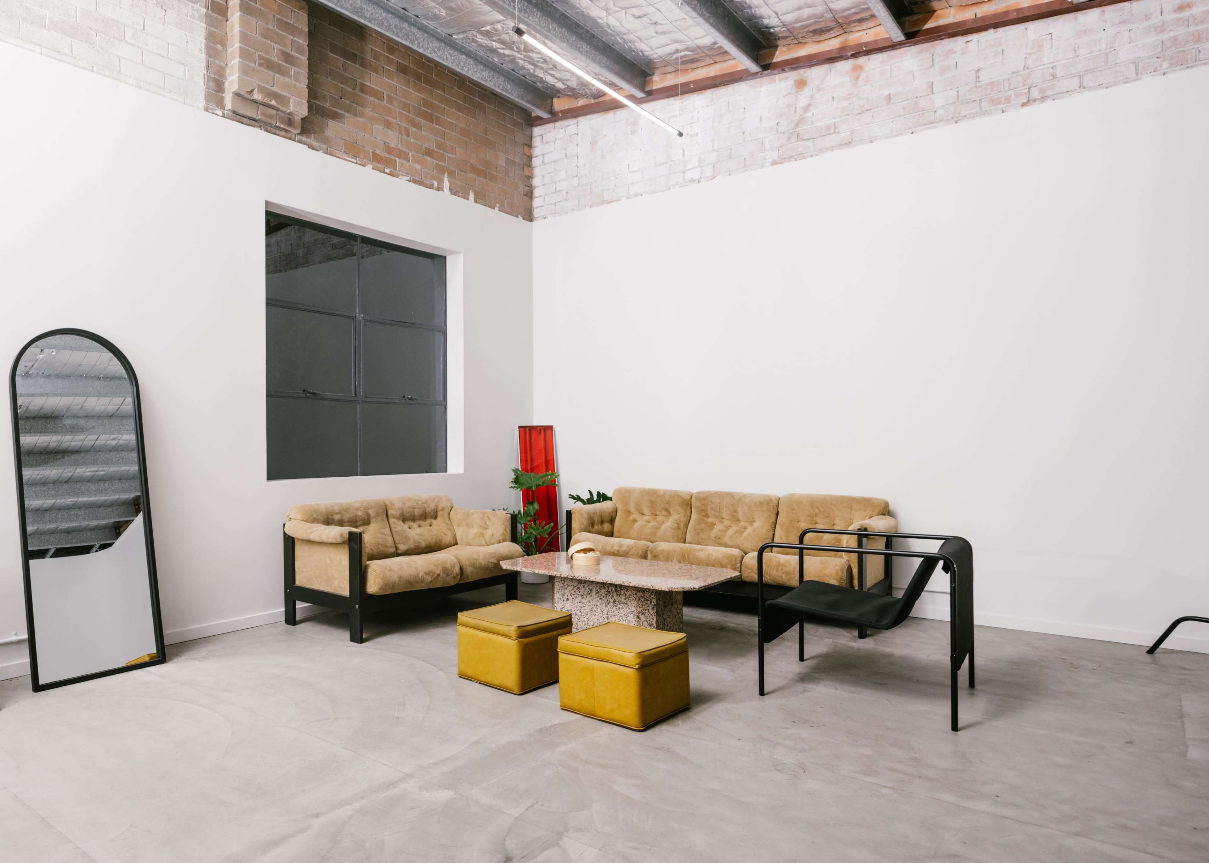 A minimalist living space with two sofas, a chair, a coffee table, and a mirror against a white wall.