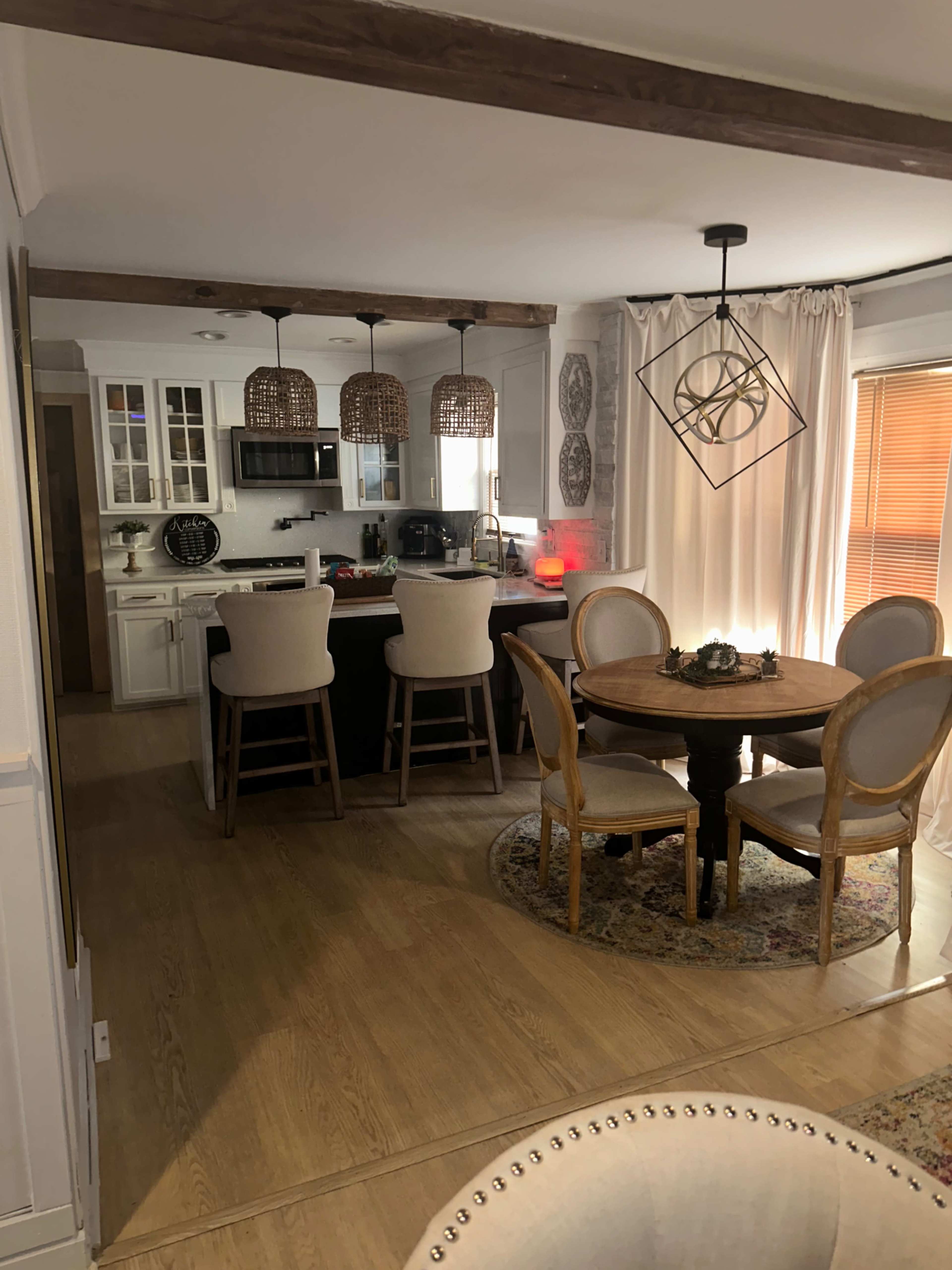 A modern kitchen and dining area with a round table and four chairs, a bar counter with stools, and decorative lighting fixtures.
