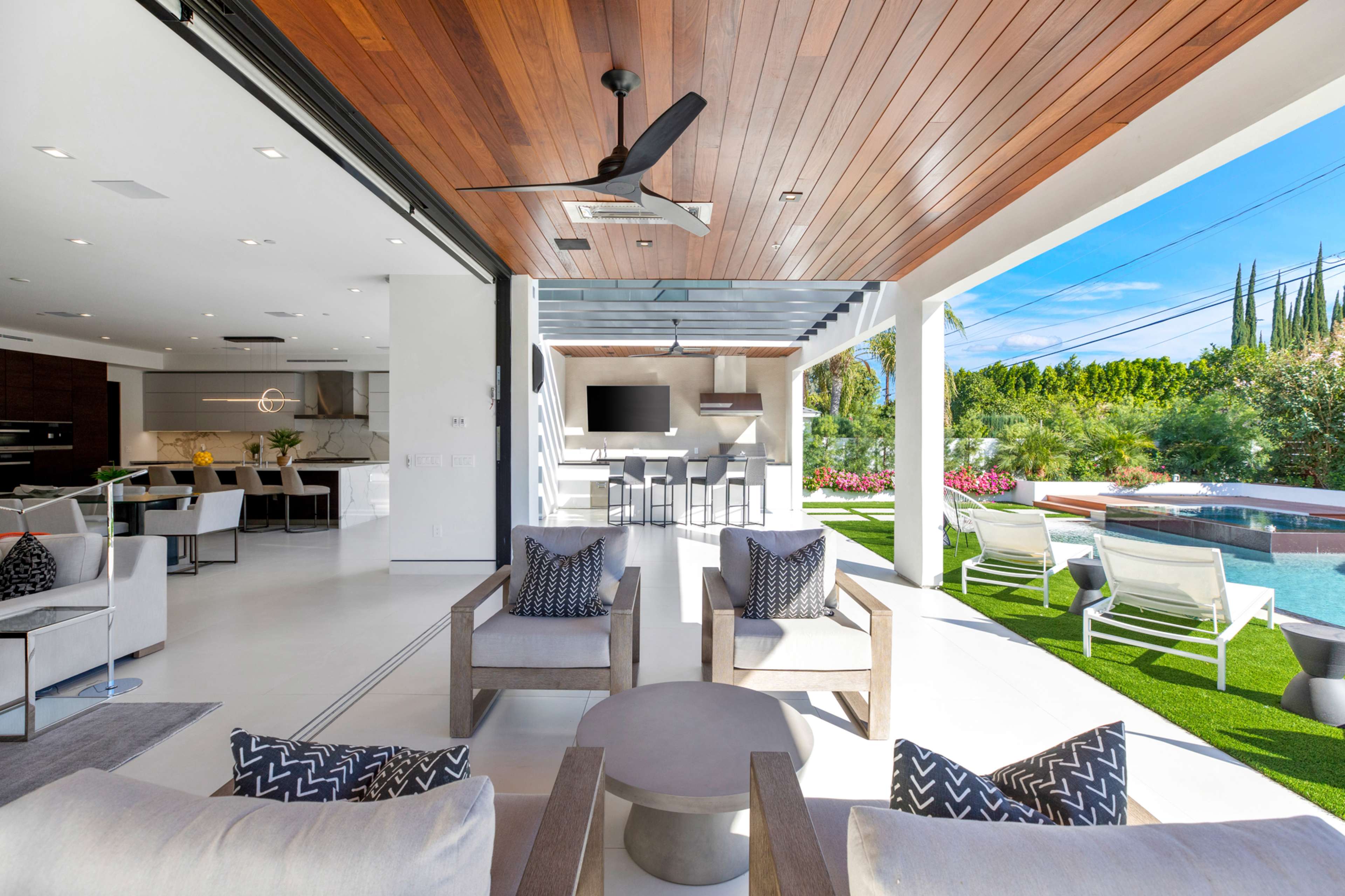 A modern outdoor living space features a seamless transition from a stylish indoor area to a poolside setting with seating and an outdoor kitchen.