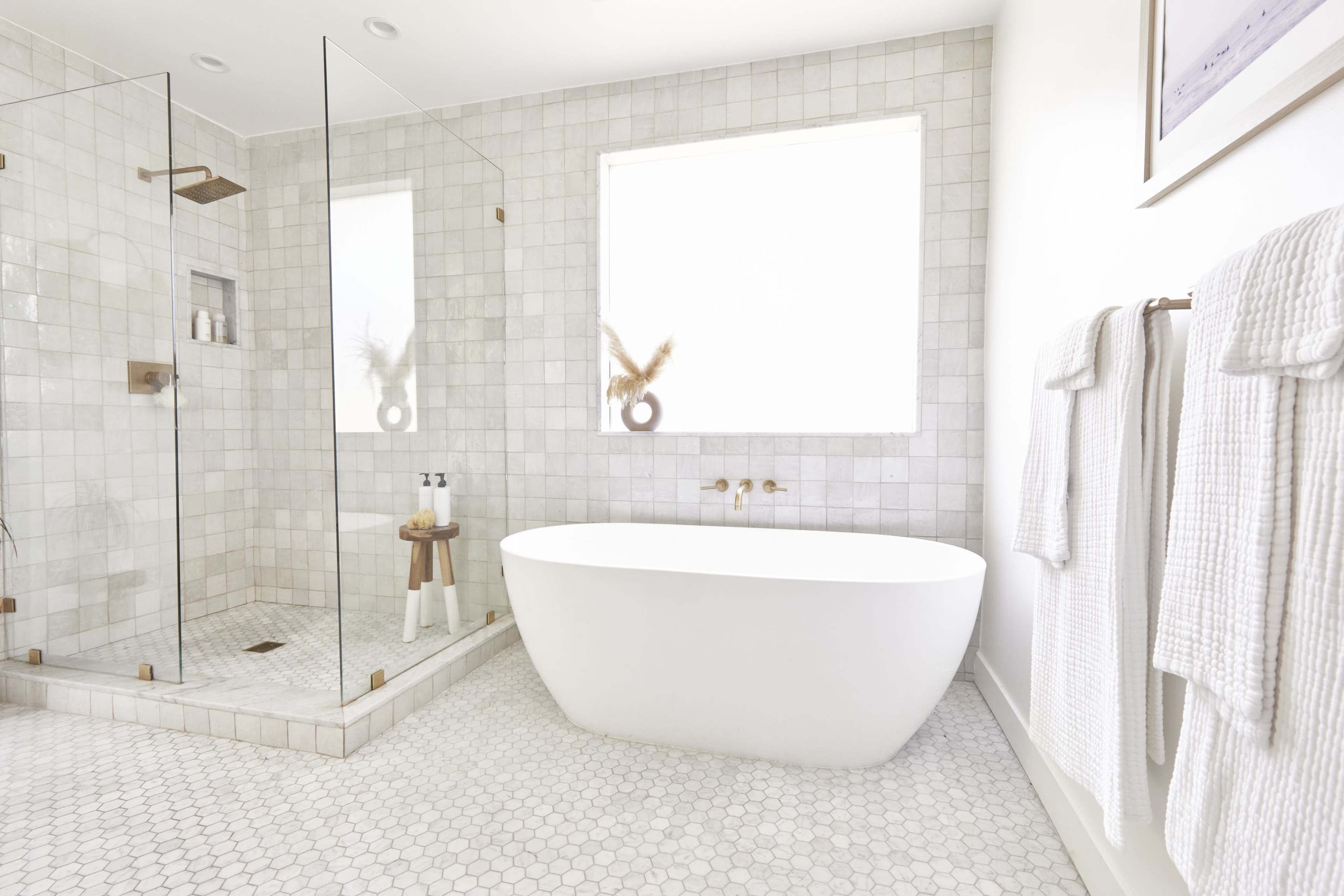 The bathroom features a freestanding white bathtub, a glass shower enclosure, and light-colored tile flooring.