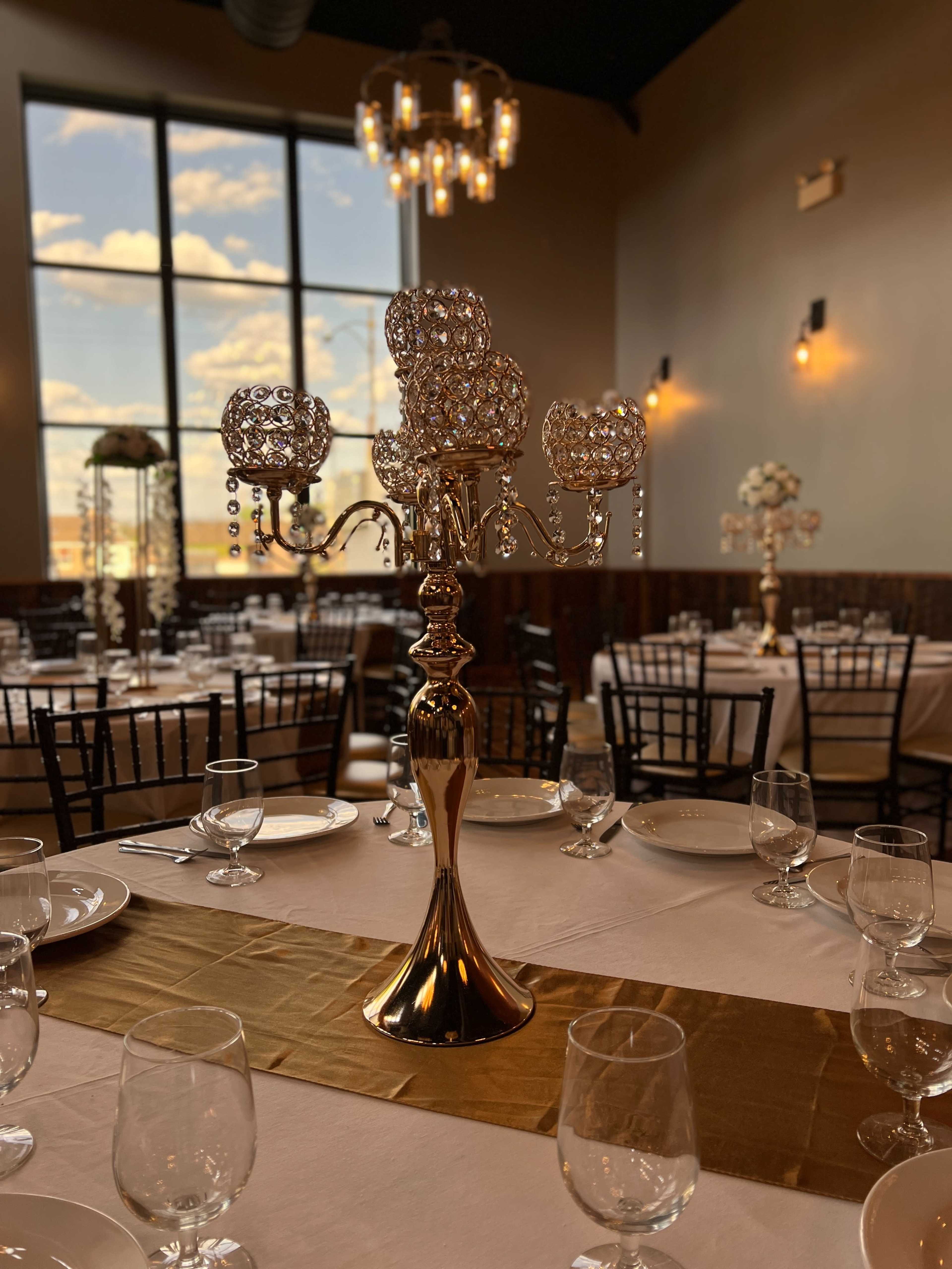 A polished table setting features a tall, ornate candelabra with crystal accents, surrounded by glasses and plates in a well-lit dining room.