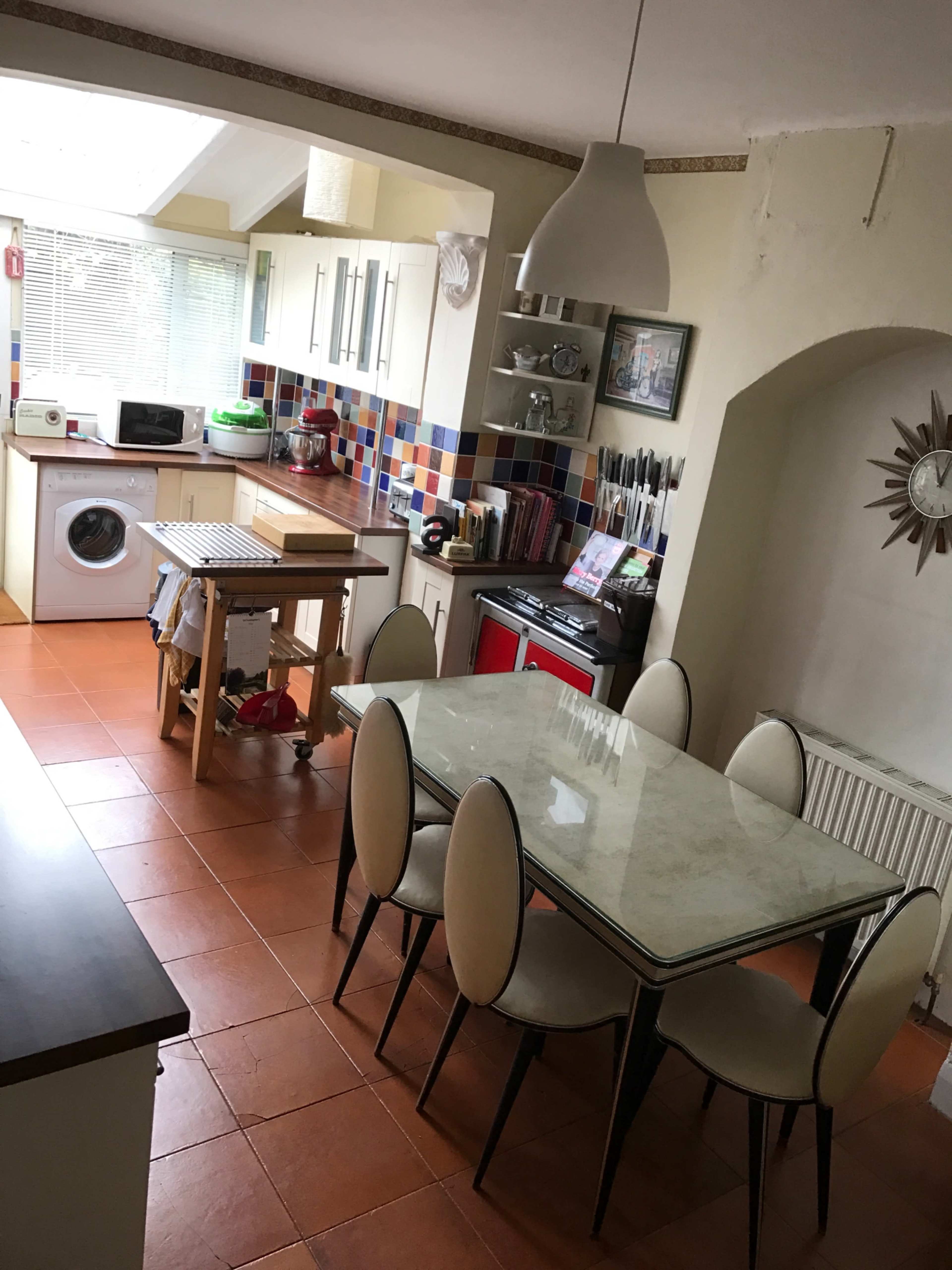 A modern kitchen with a dining table set for six, featuring a washing machine and various kitchen appliances along the walls.