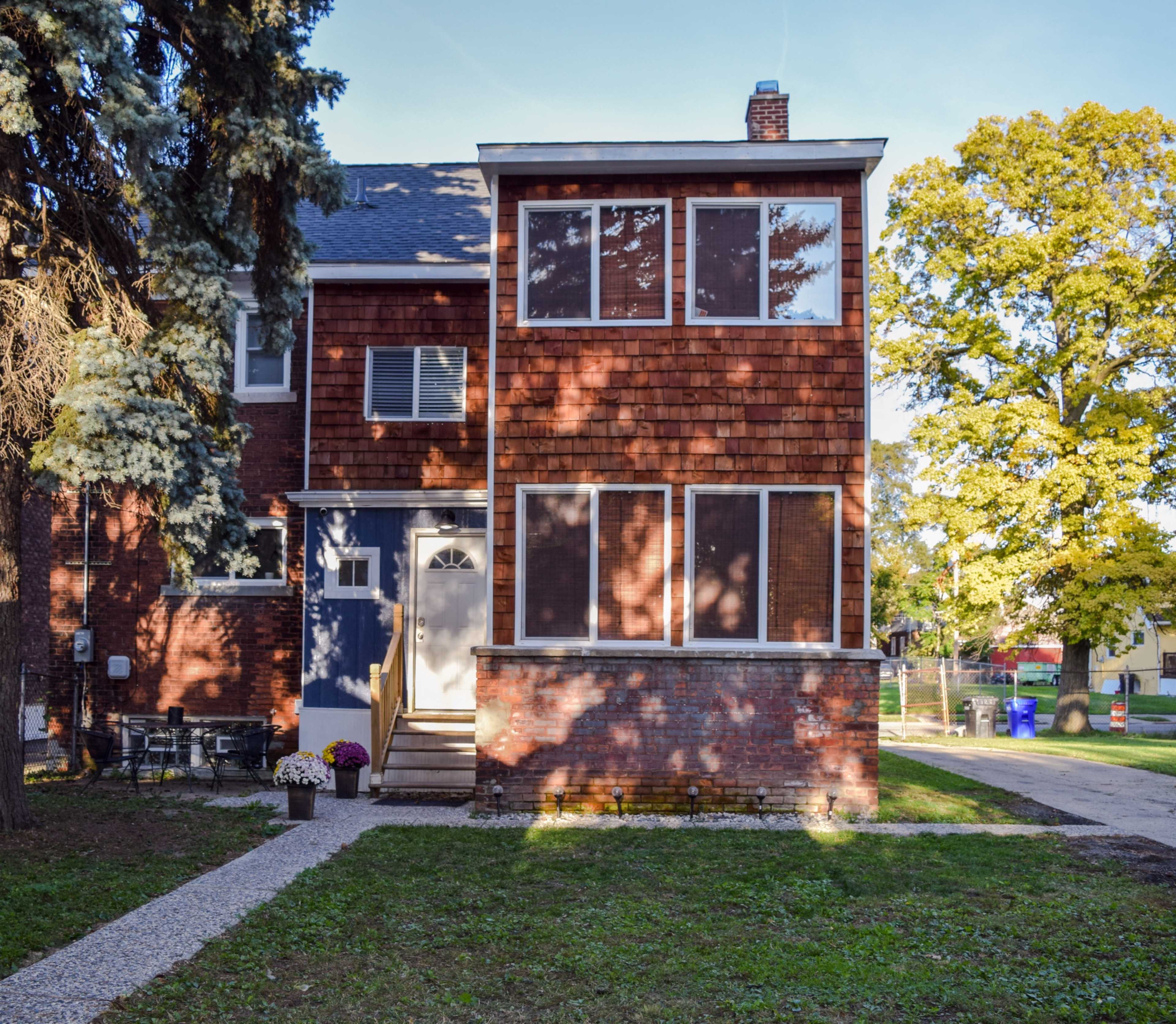 A two-story brick and wooden townhouse features multiple windows and a gravel pathway leading to the entrance.