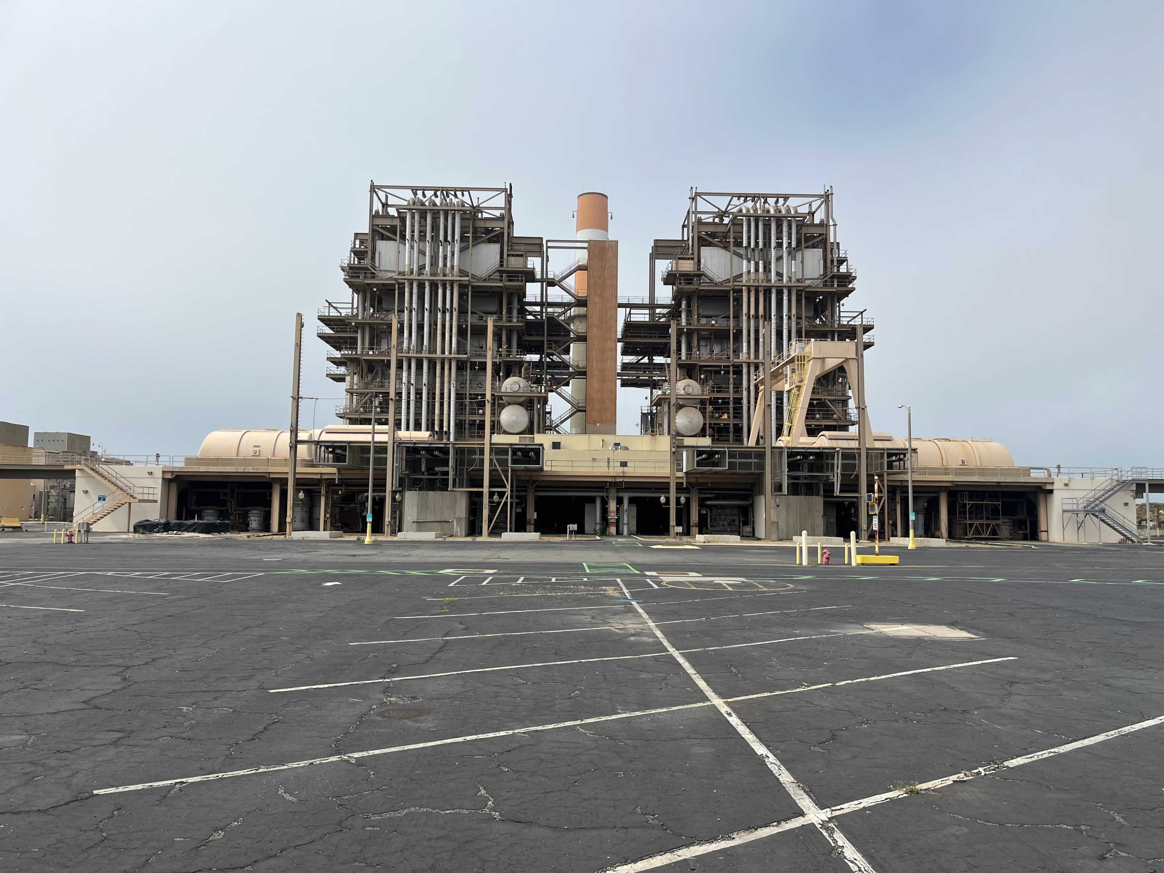 A power plant with large industrial structures and cooling towers, set against a cloudy sky.