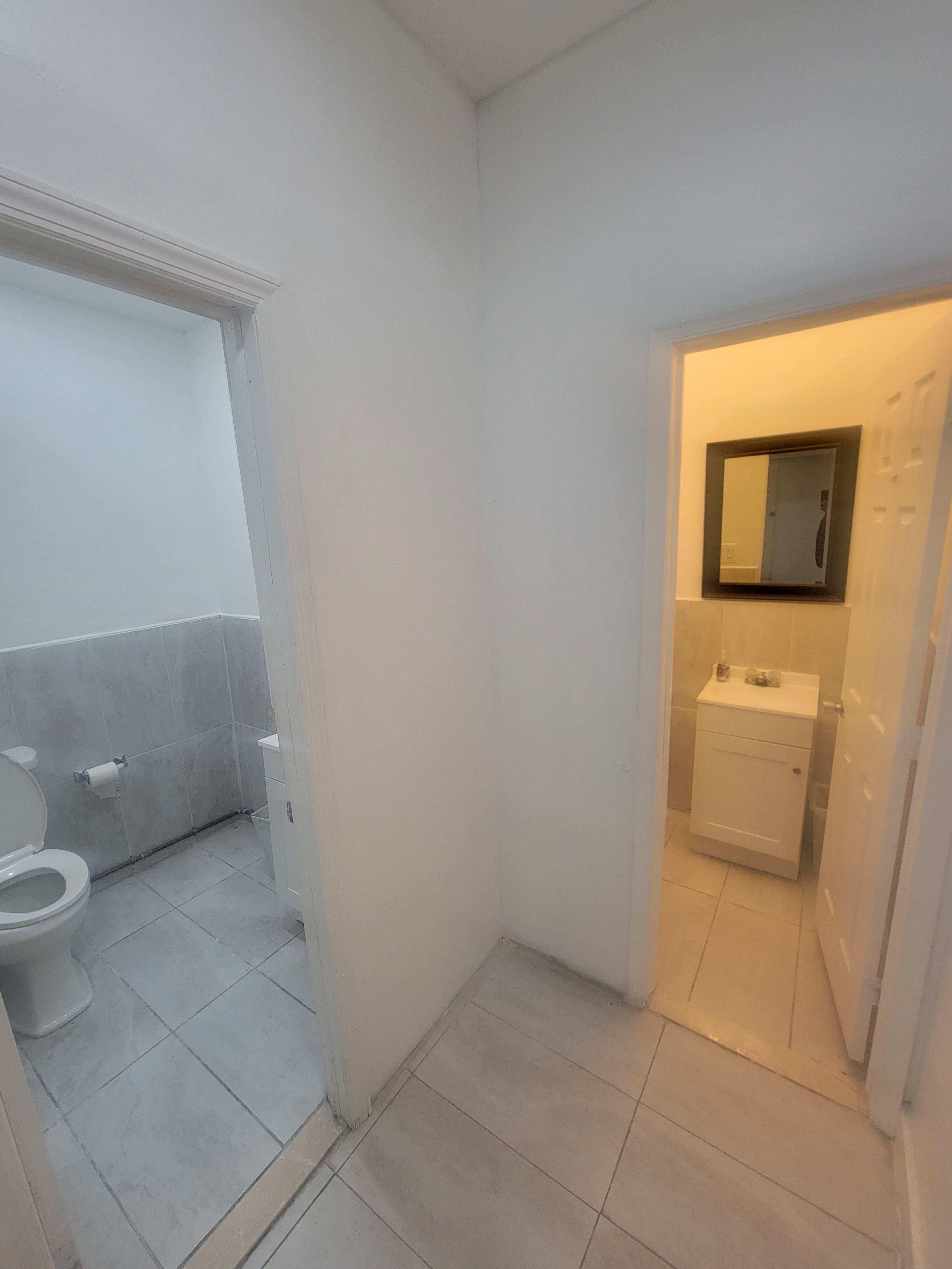 A bathroom area with two doorways: one leading to a toilet and the other to a sink with a mirror.