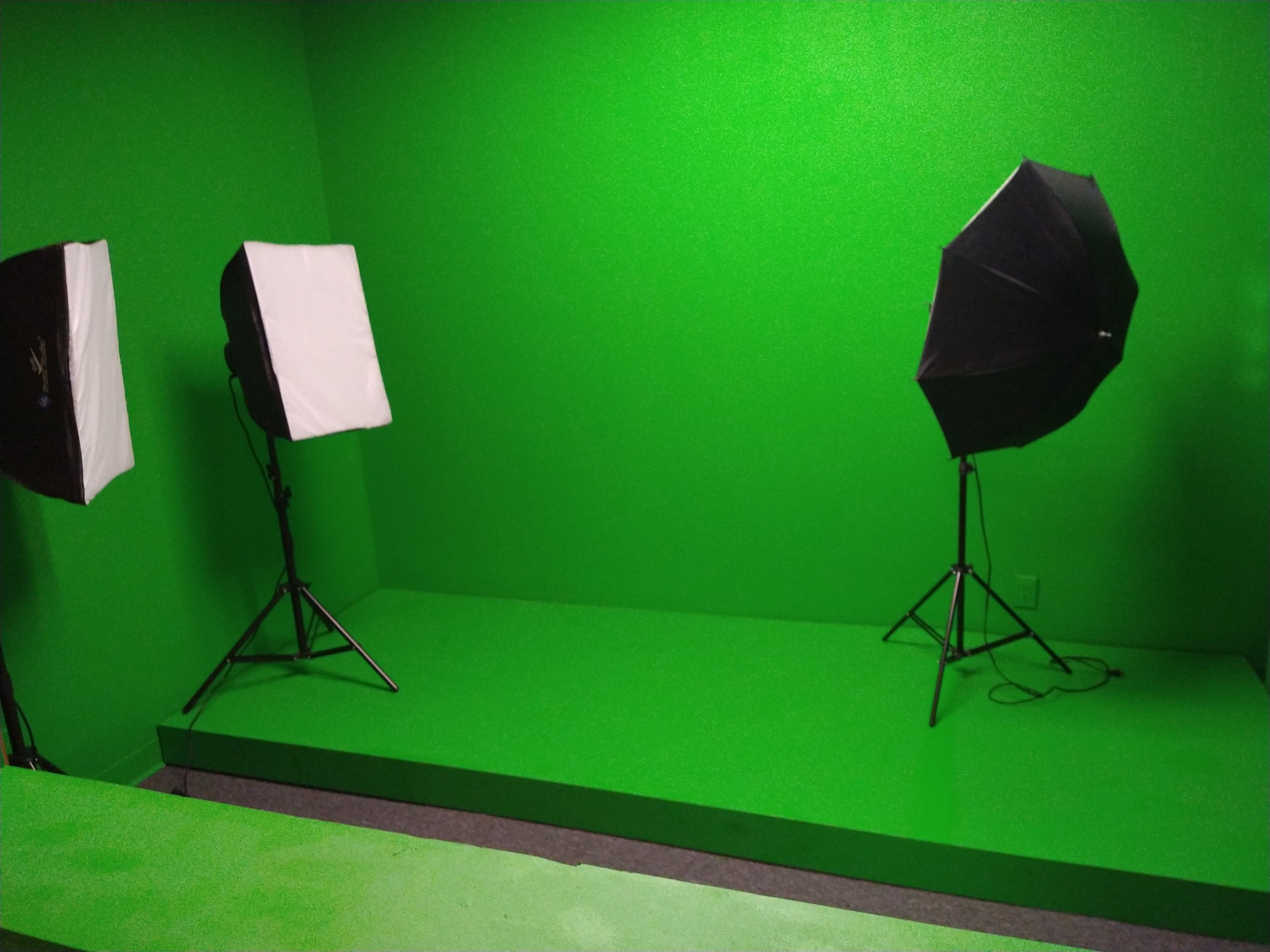 The image shows a green screen studio featuring two lights on tripods and a raised green platform.