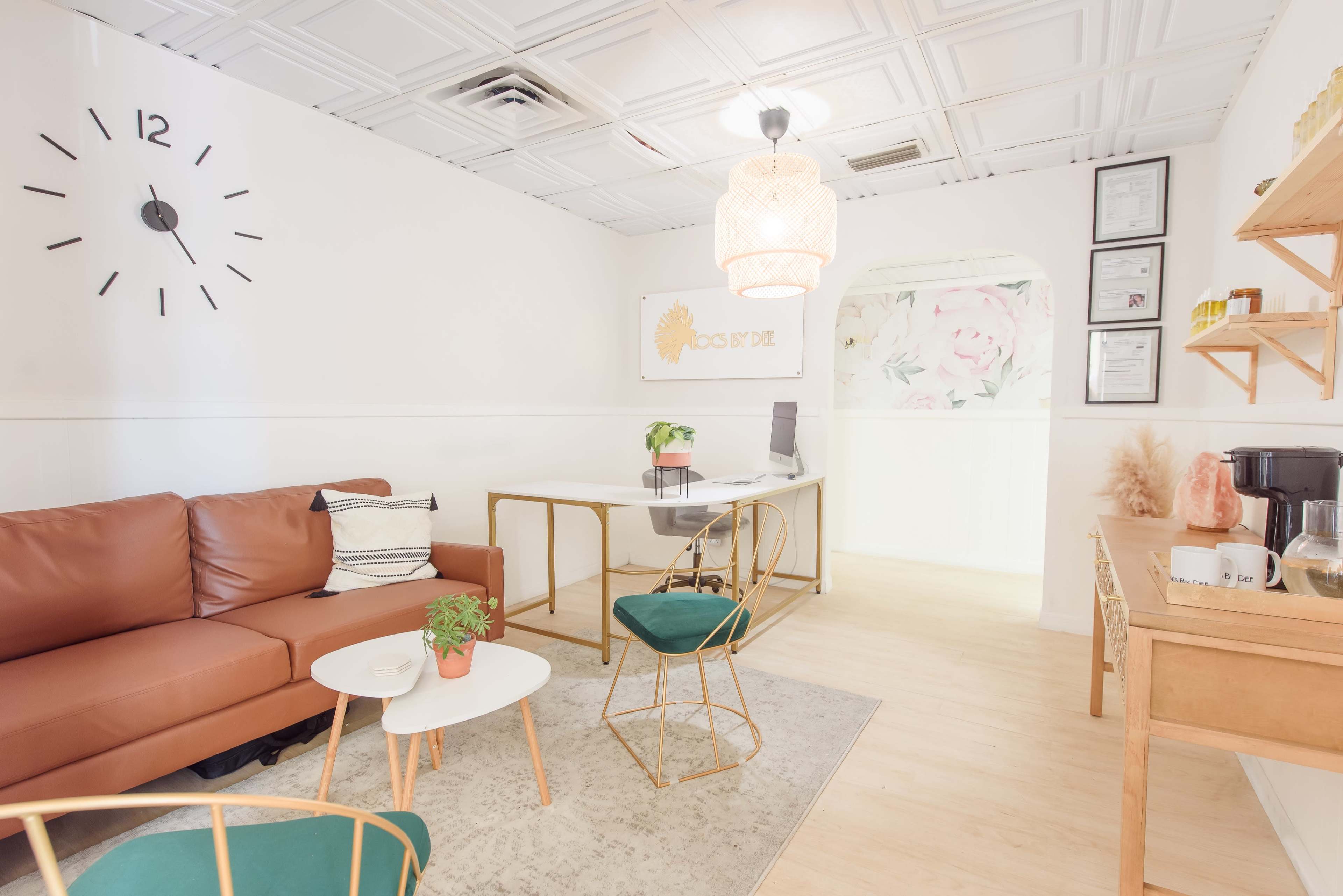 A modern, well-lit reception area with a brown leather sofa, a glass desk, and decorative plants.