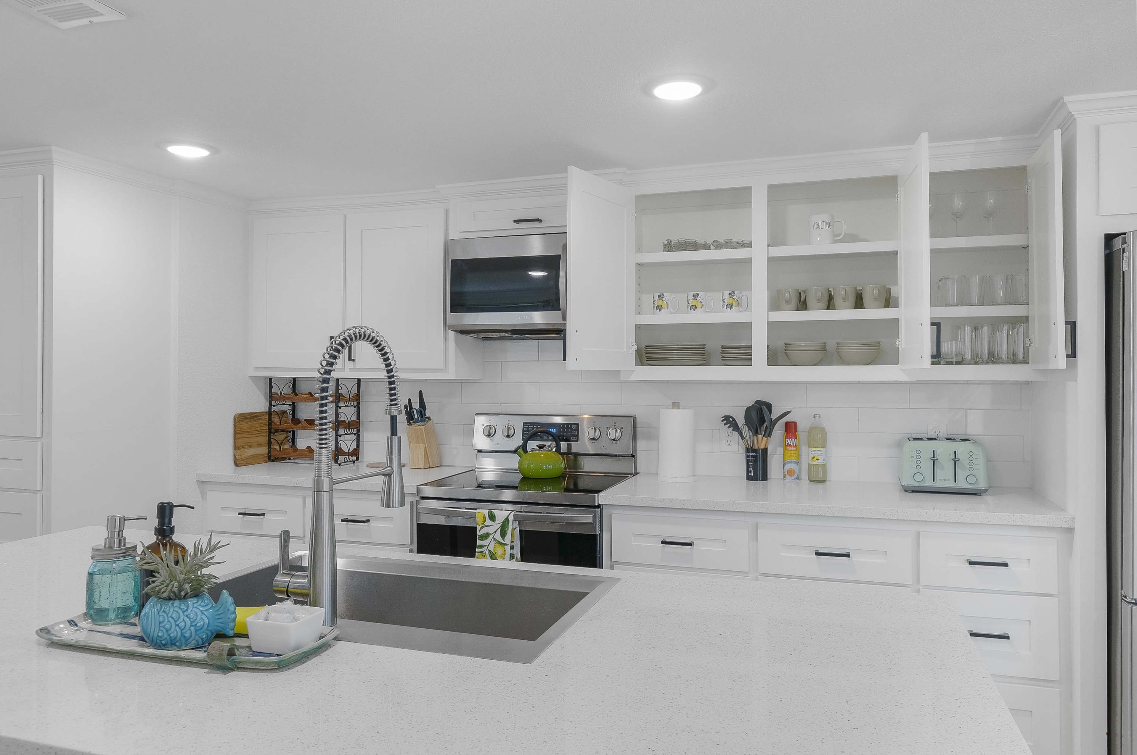 A modern kitchen features white cabinetry, stainless steel appliances, and a central island with a sink and countertop space.