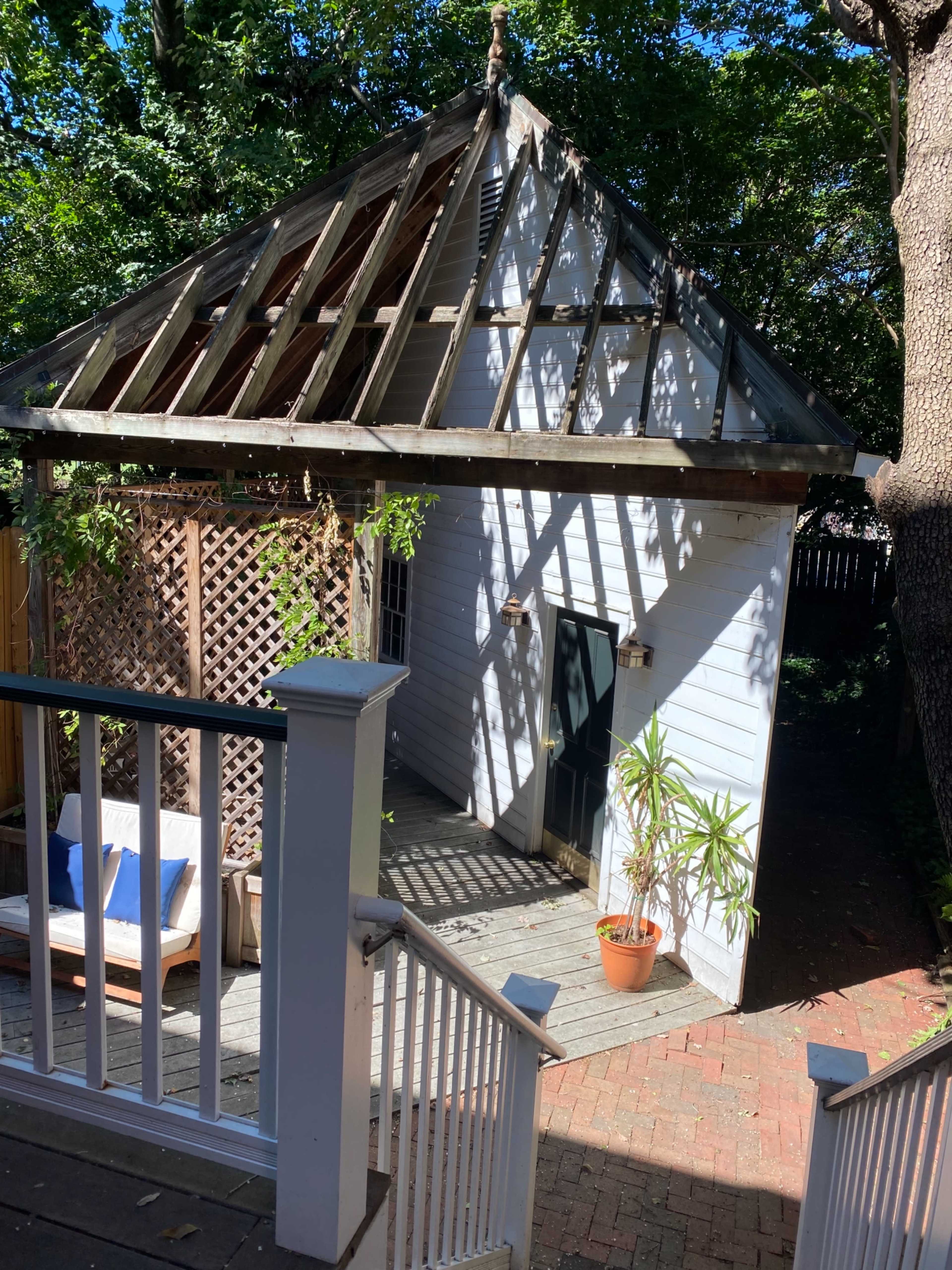 A small, partially constructed building with an open roof sits at the end of a garden path, surrounded by greenery.