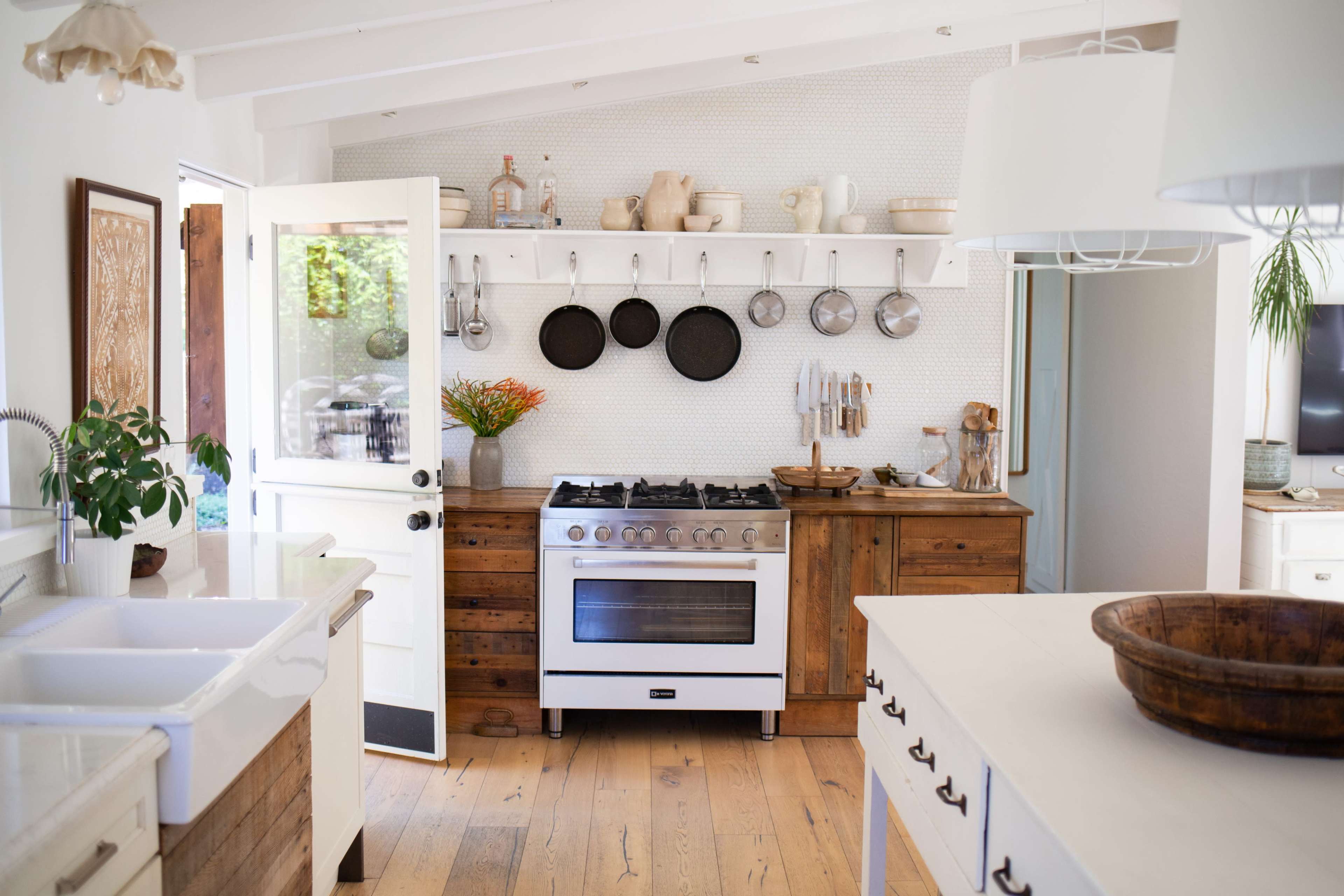 A clean, modern kitchen features a white stove, wooden cabinetry, and pots hanging on a wall.