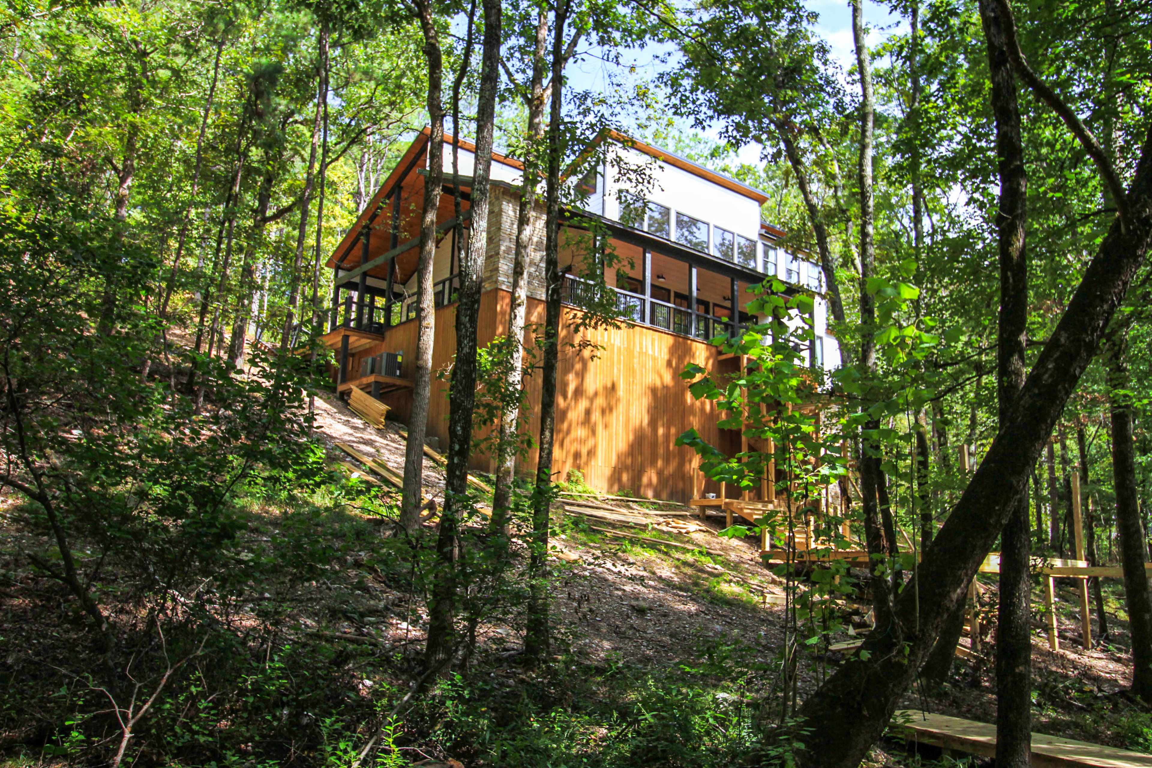 A modern house sits on a sloped hillside, surrounded by trees.