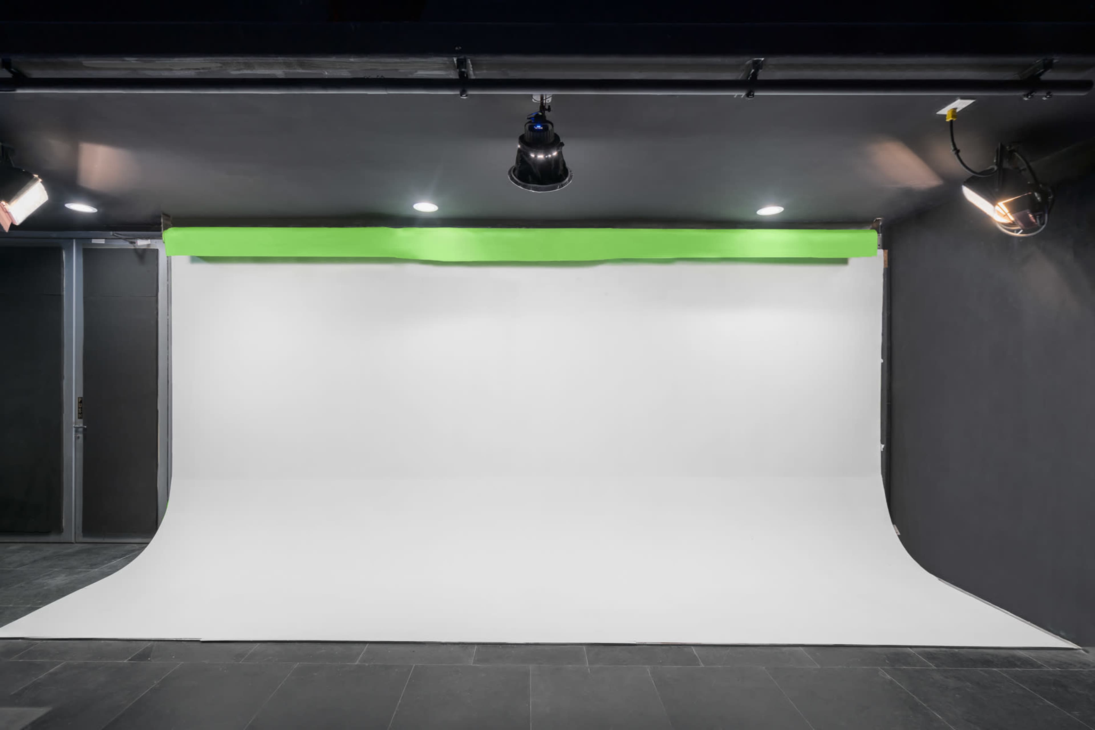 A photography studio with a white backdrop and green screen, illuminated by multiple overhead lights.