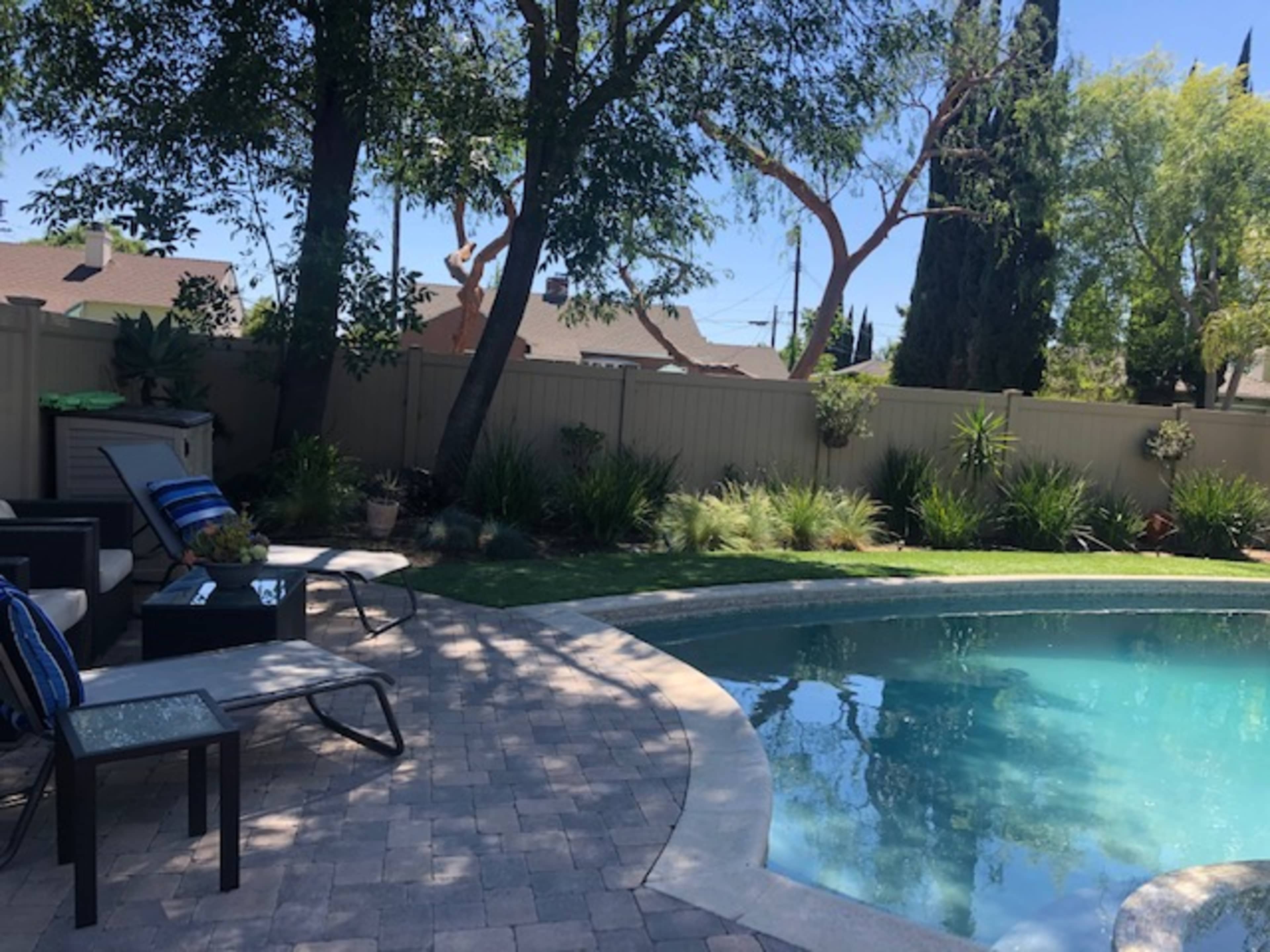 The image shows a backyard with a swimming pool surrounded by lounge chairs and greenery.