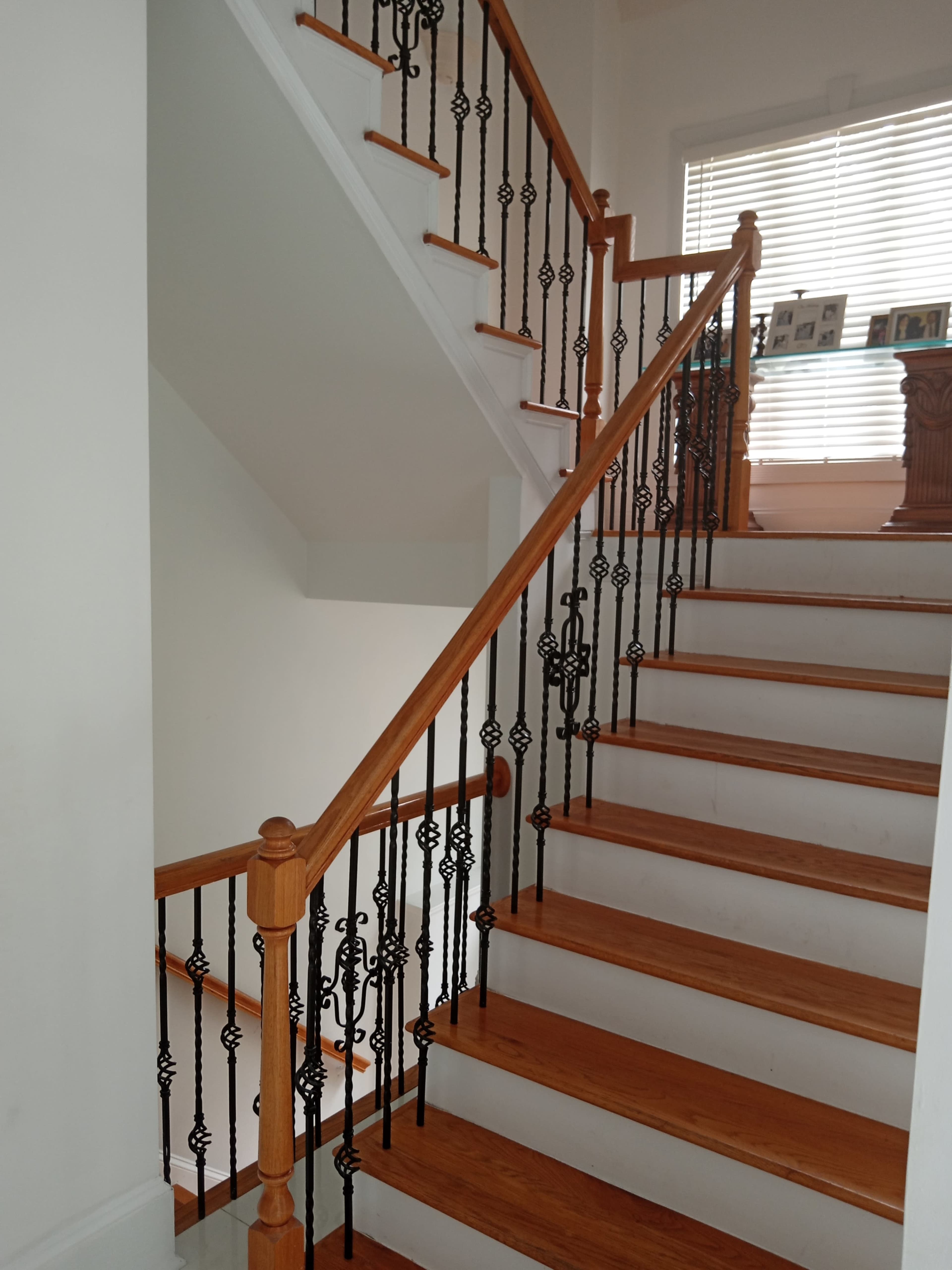 A wooden staircase with a black wrought iron railing and a large window permitting light onto the upper landing.