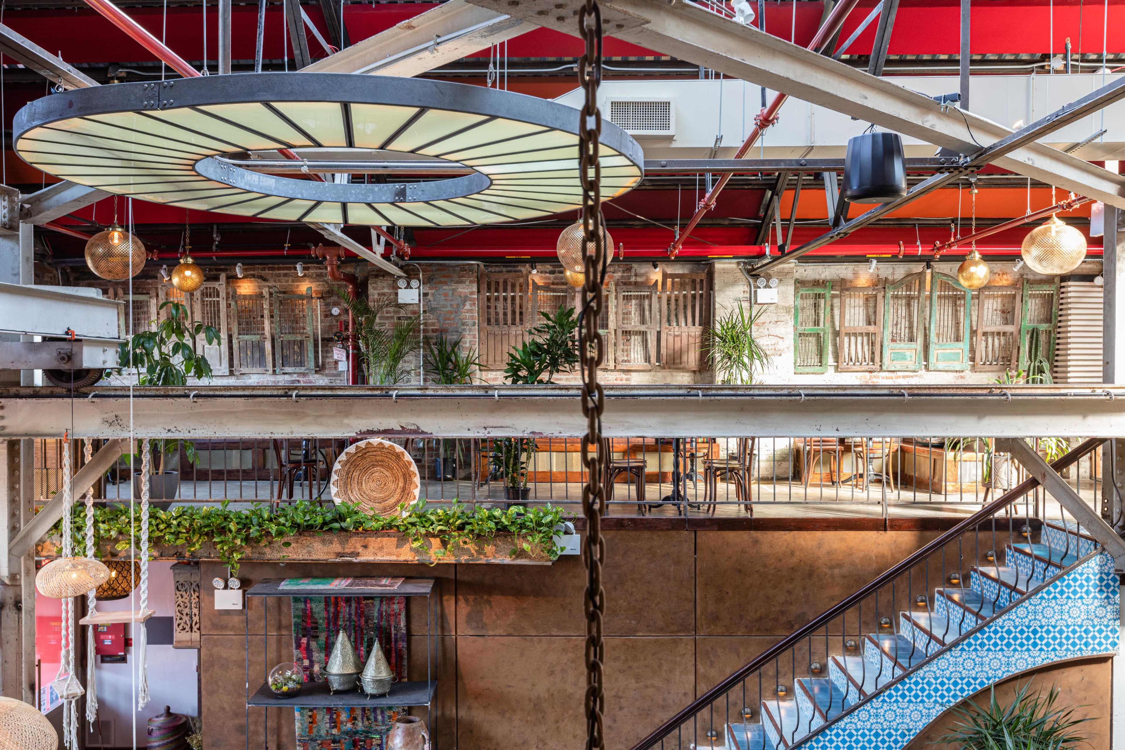 A multi-level industrial-style interior space with hanging lights, green plants, decorative elements, and a blue-tiled staircase.