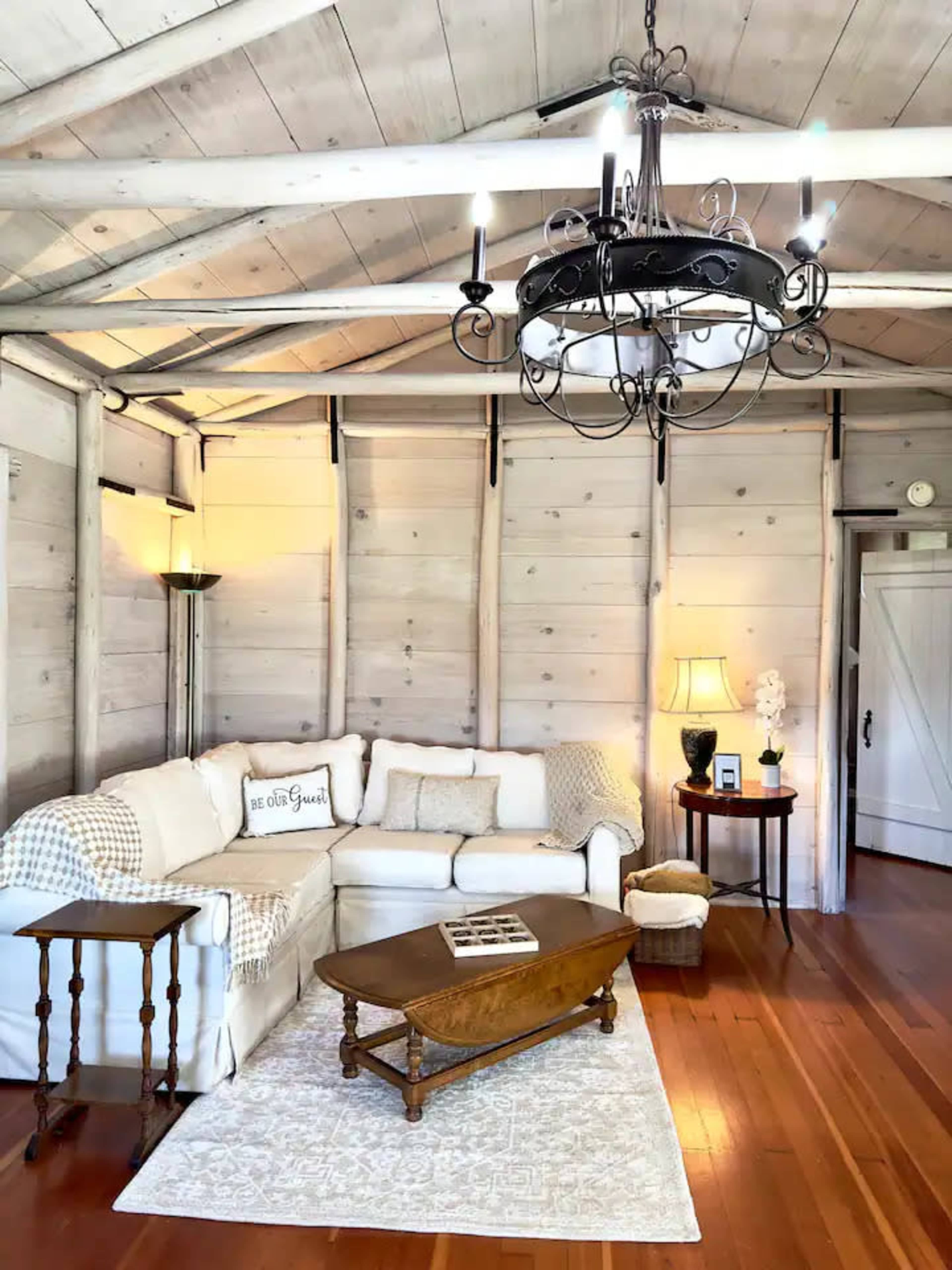 A cozy living room with a white couch, wooden coffee table, and a chandelier, all set against a backdrop of wooden paneled walls.