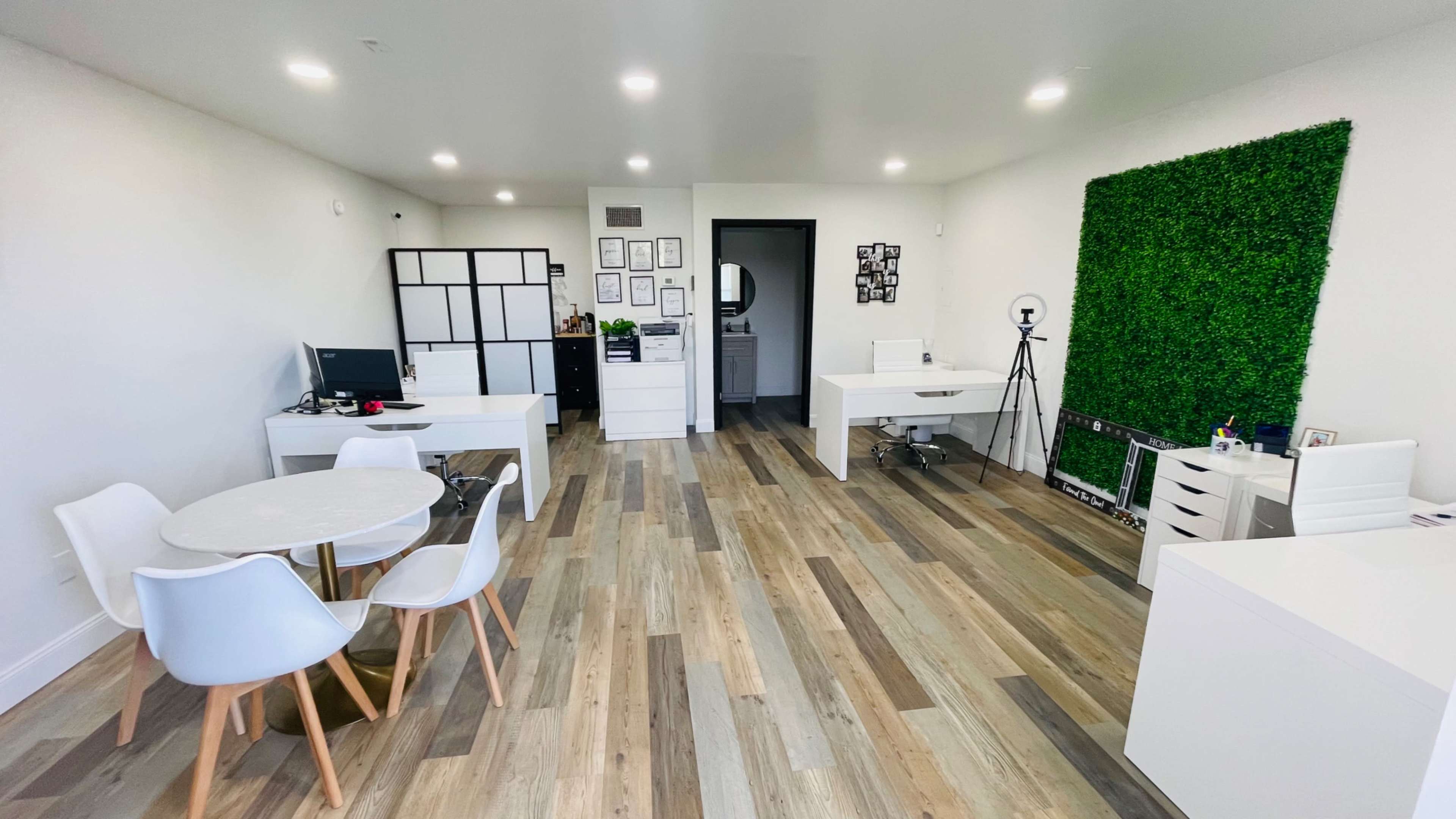 A modern office space with white furniture, wooden flooring, and a green wall feature.